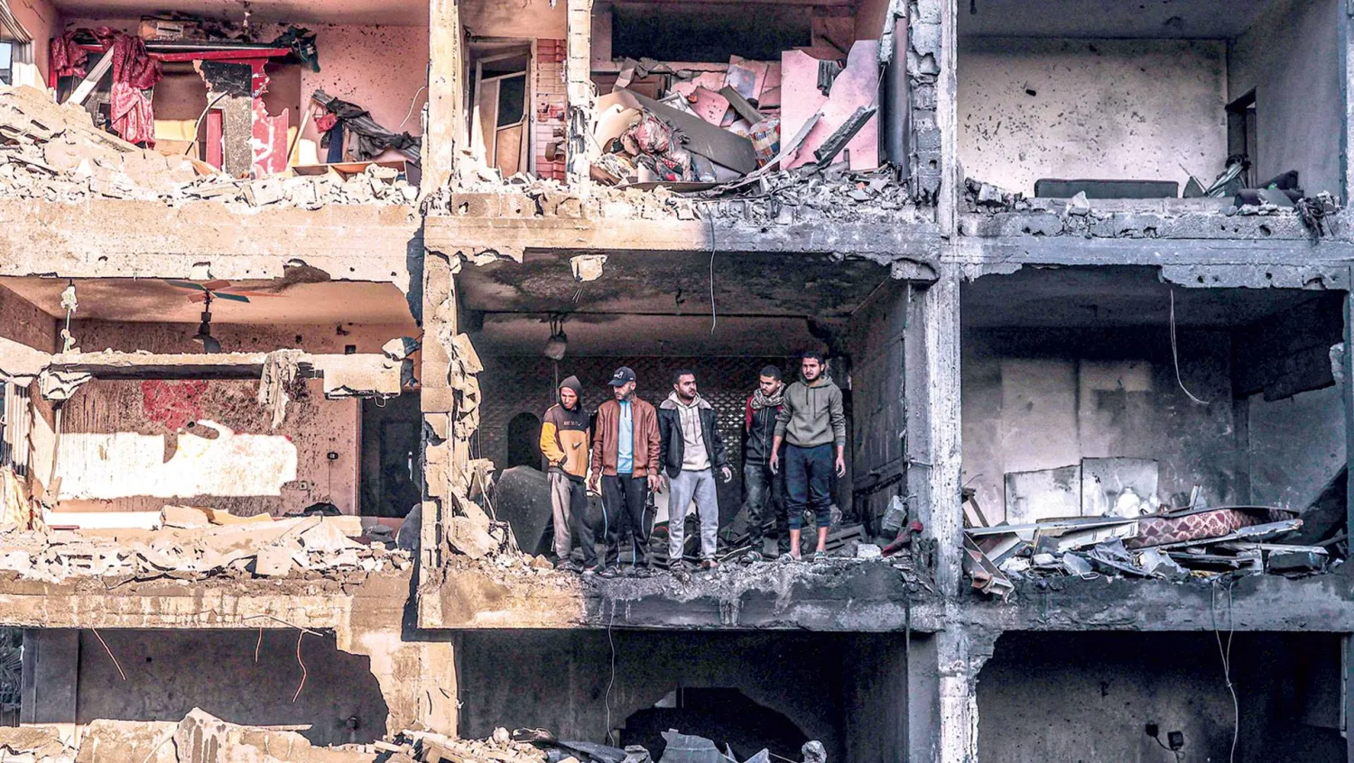  فلسطينيون يعاينون بناية مدمرة بعد قصف إسرائيلي على رفح جنوب قطاع غزة أمس (أ.ف.ب)