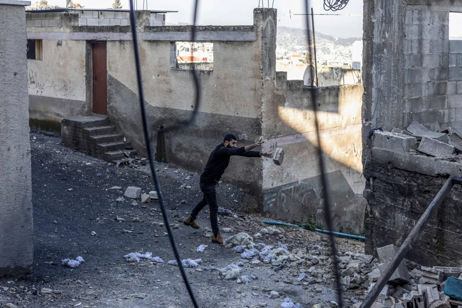 فلسطيني يزيح الركام أمام منزله في مخيم جنين بالضفة الغربية (أ.ف.ب)