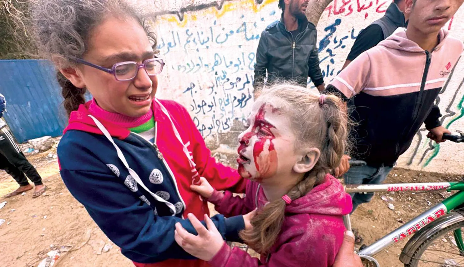  طفلة فلسطينية تساعد أخرى مصابة بعد غارة إسرائيلية على منطقة الزوايدة وسط قطاع غزة أمس (أ.ب)