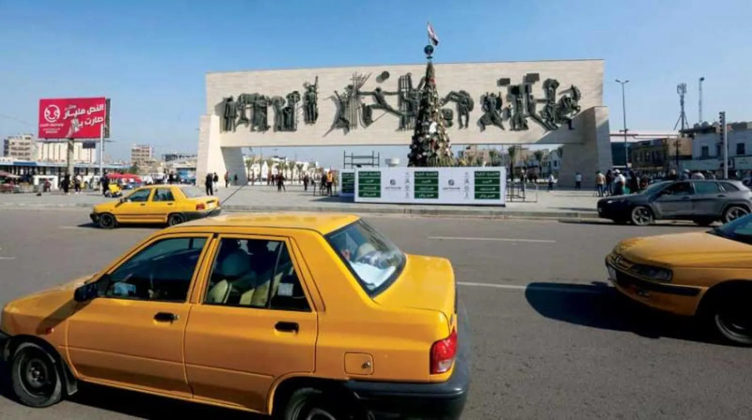 سيارات أجرة عراقية تمر بشجرة عيد الميلاد في ساحة التحرير ببغداد وتظهر صور لأعضاء من الحشد الشعبي متضمنة المهندس وسليماني (أ.ف.ب)