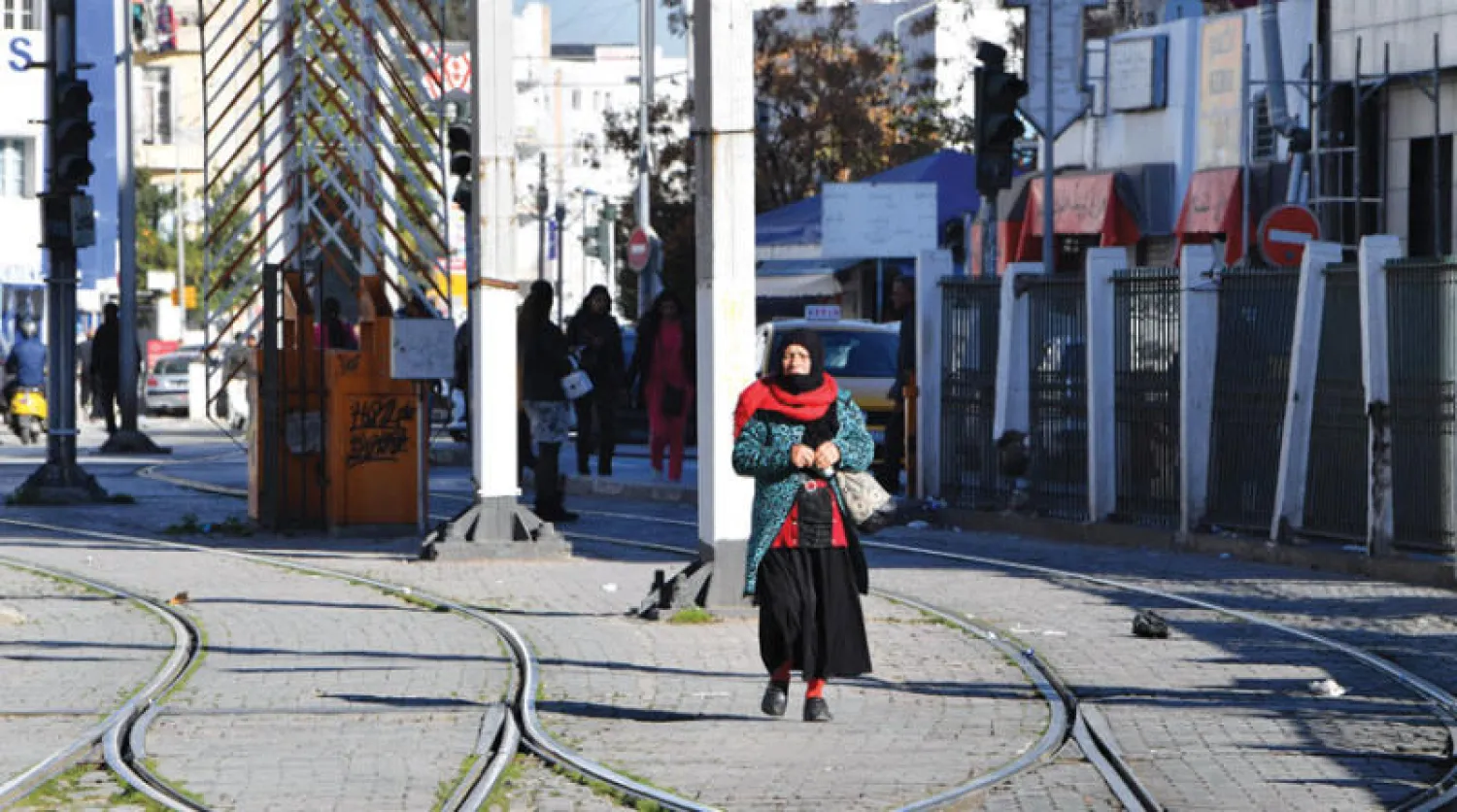 تونسية تسير فوق أحد خطوط الترام عقب تنظيم إضراب واسع بقطاع النقل في العاصمة يوم الاثنين (أ.ف.ب)