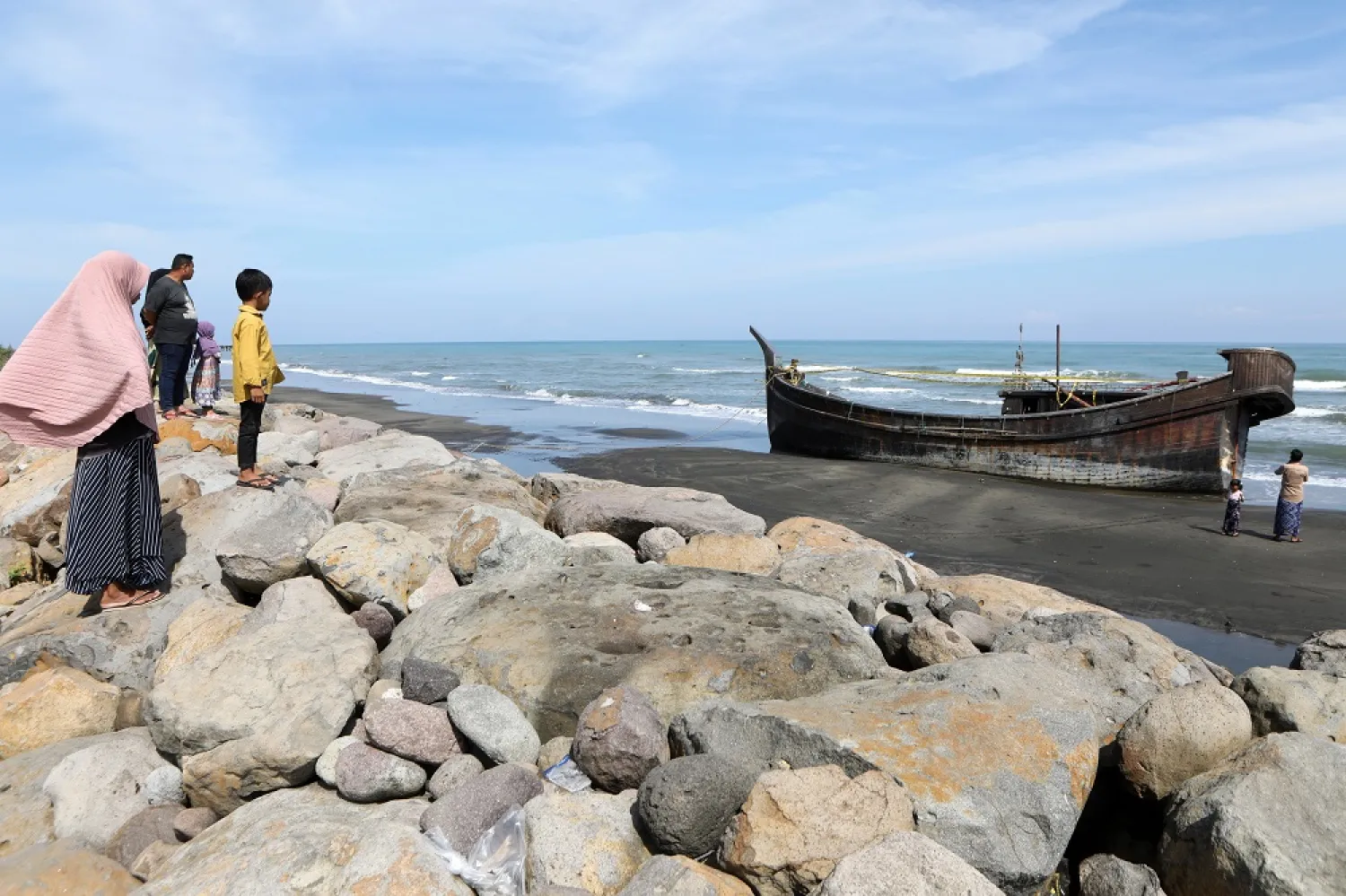 People look at a Rohingya refugee boat stranded at the beach in Pidie, Aceh, Indonesia, 28 December 2022. (EPA)