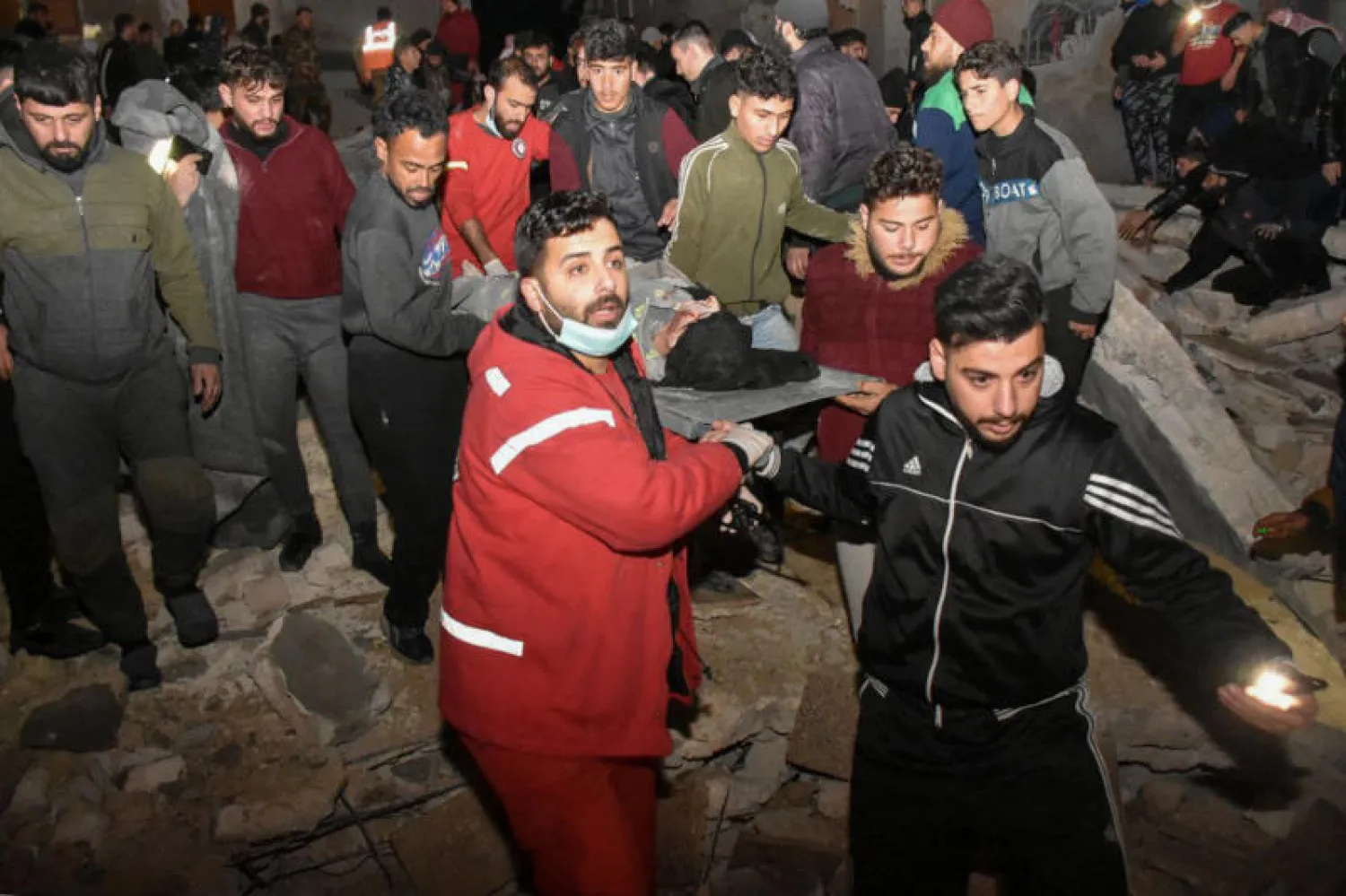 عمال الإنقاذ وأشخاص يحملون جريحاً من تحت أنقاض مبنى من 8 طوابق مدمر في حي الأربعين بمدينة حماة (د.ب.أ)