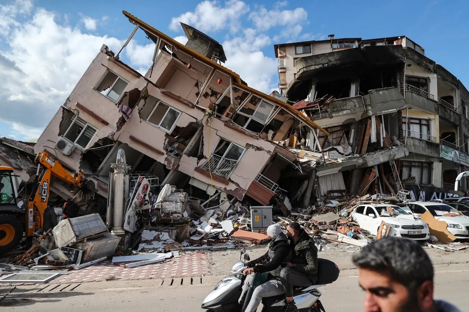 People pass in front of a collapsed building in Hatay, Türkiye, 07 February 2023. (EPA)