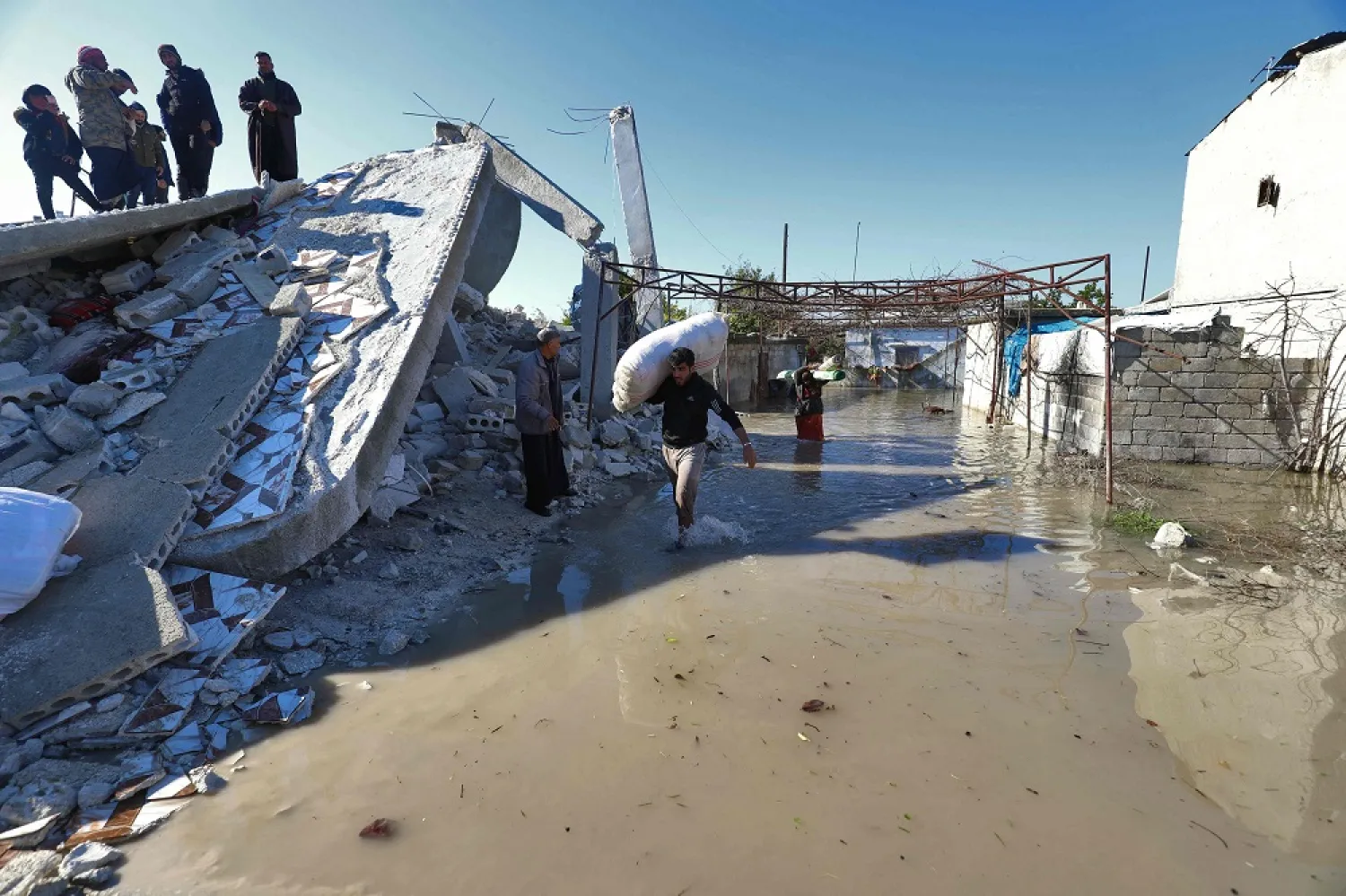 A Syrian man carries a sac past a destroyed building in a flooded area after the collapse of a dam on the Orontes (Assi) river near al-Tulul village in Salqin, in Syria's opposition-held Idlib province, near the border with Türkiye, on February 9, 2023 following a deadly earthquake. (AFP)
