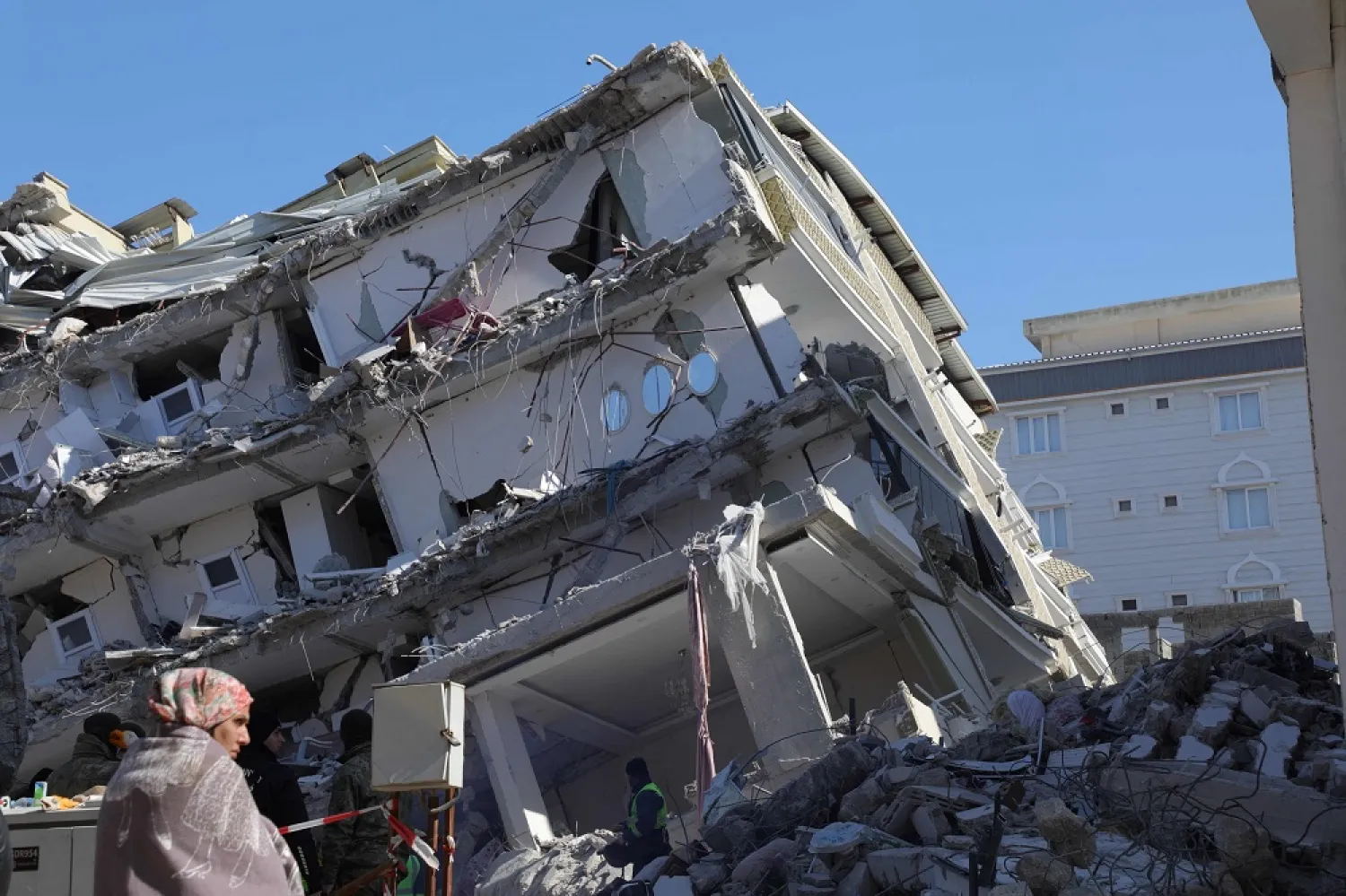 A woman stand in front of a a collapsed building in Islahiya, in the hard hit region of Gaziantep, on February 11, 2023, five days after a 7.8 magnitude earthquake struck the border region of Türkiye and Syria. (AFP) 