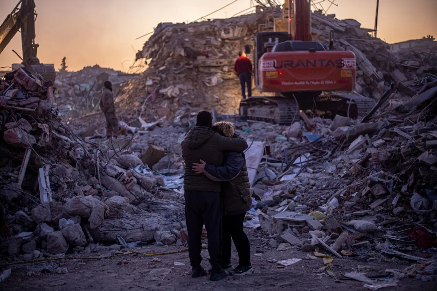 People hug each other in front of collapsed buildings after a powerful earthquake, in Hatay, Türkiye, 14 February 2023. (EPA)
