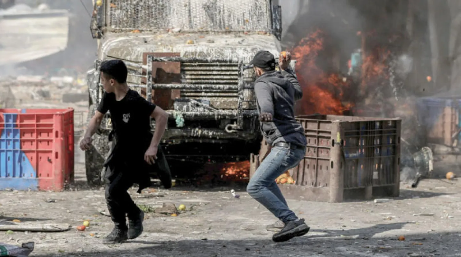 شابان فلسطينيان أمام مركبة للجيش الإسرائيلي خلال مواجهات في نابلس الأربعاء (د.ب.أ)