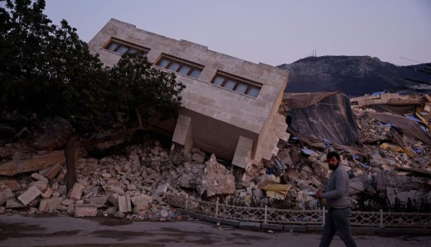 A man walks by a collapsed building and rubble, in the aftermath of a deadly earthquake, in Antakya, Hatay province, Türkiye, February 21, 2023. REUTERS/Clodagh Kilcoyne