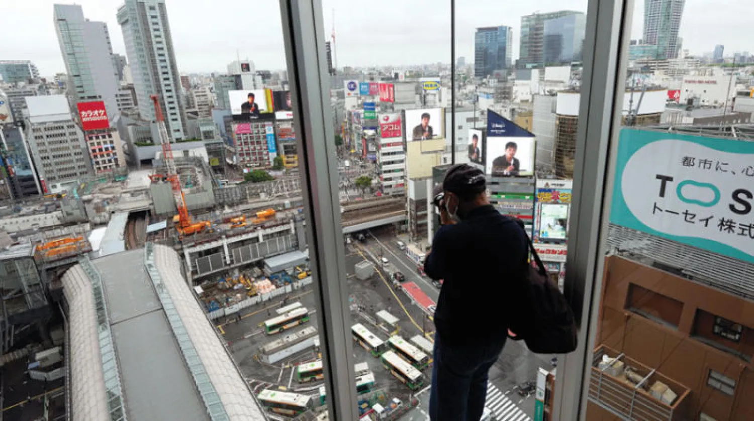 رجل يلتقط صورة لمنطقة شيبويا من منصة مراقبة في طوكيو (أ.ب)
