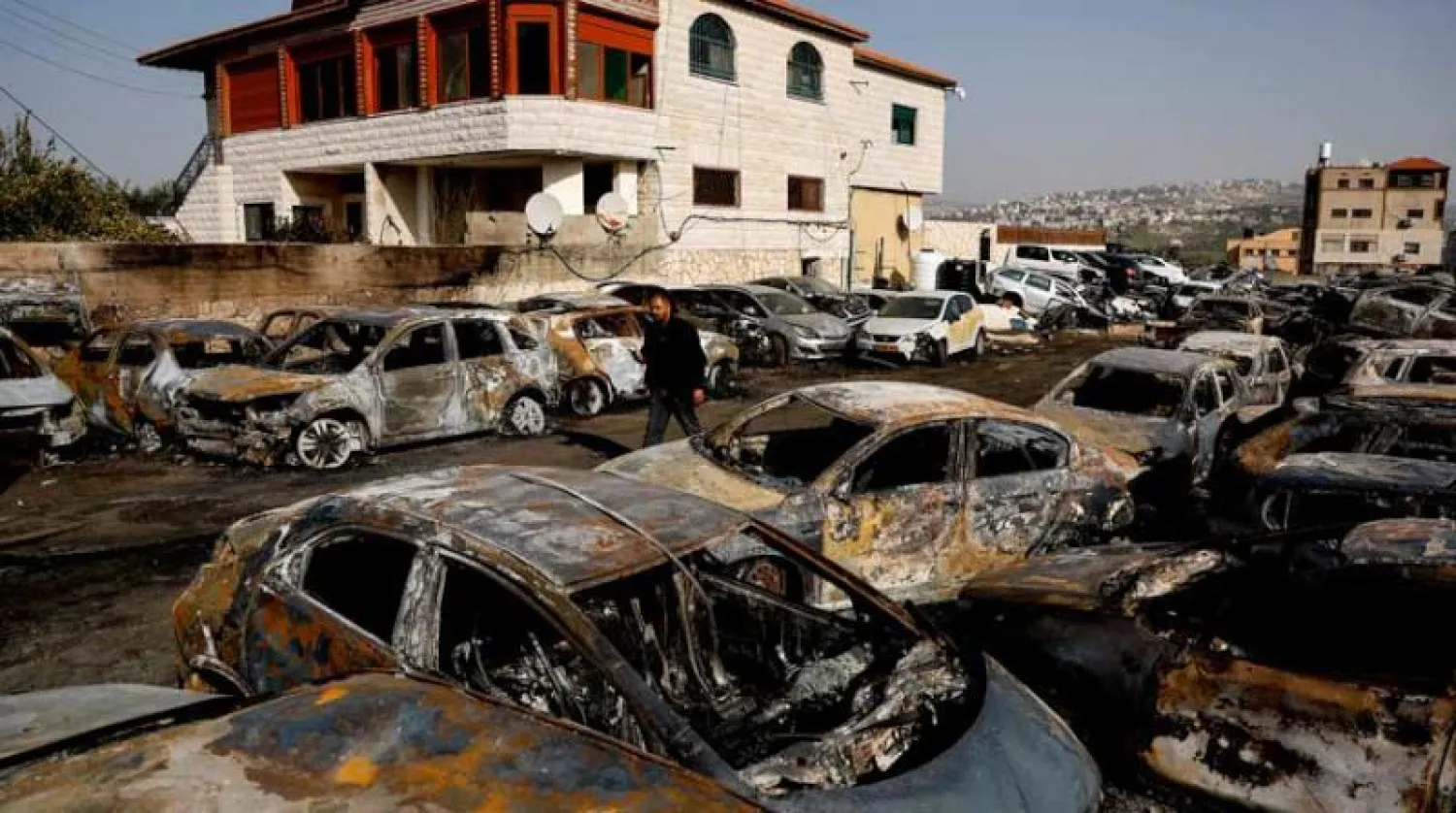 رجل يعبر بين سيارات احترقت بهجوم نفذه مستوطنون بالقرب من حوارة في الضفة الغربية (رويترز)