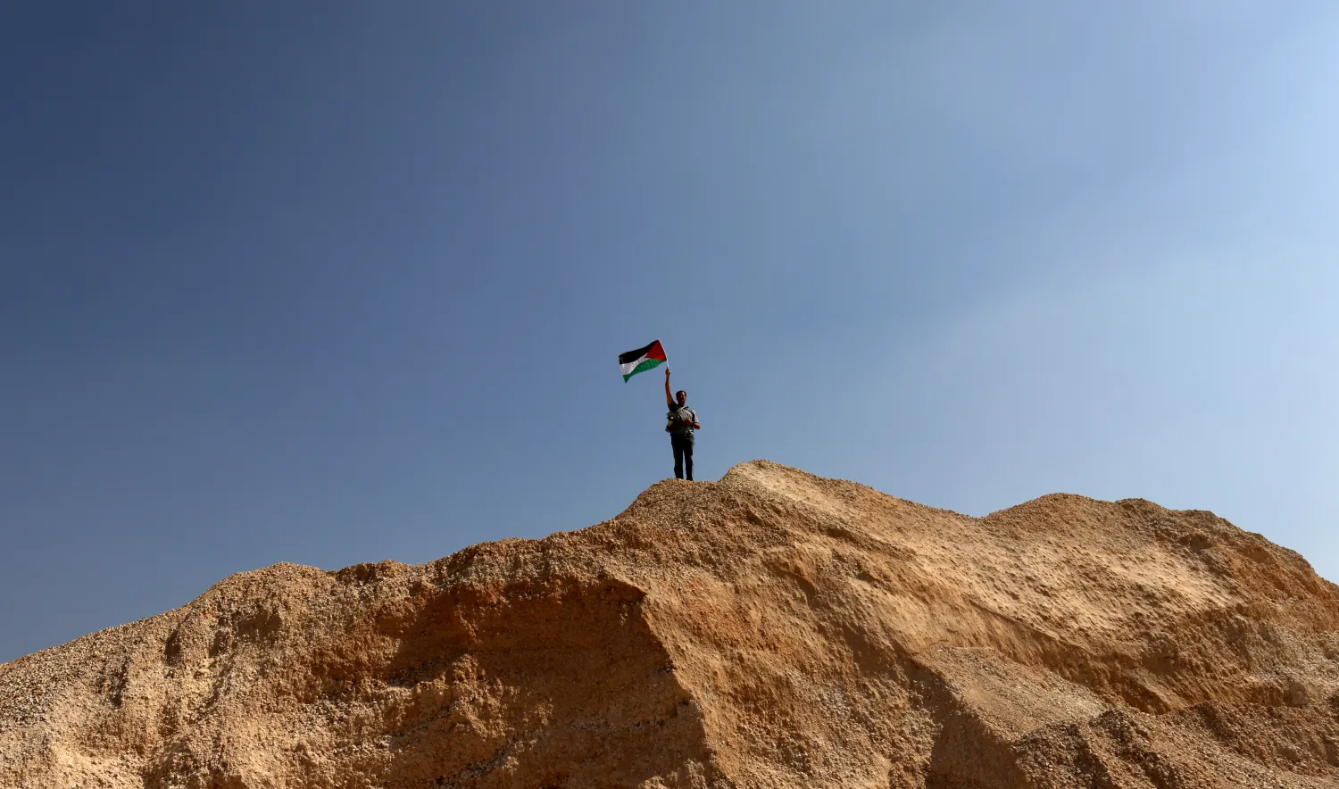 رجل يلوح بالعلم الفلسطيني خلال مظاهرة عند مدخل قرية حوارة بالضفة الغربية (إ.ب.أ)