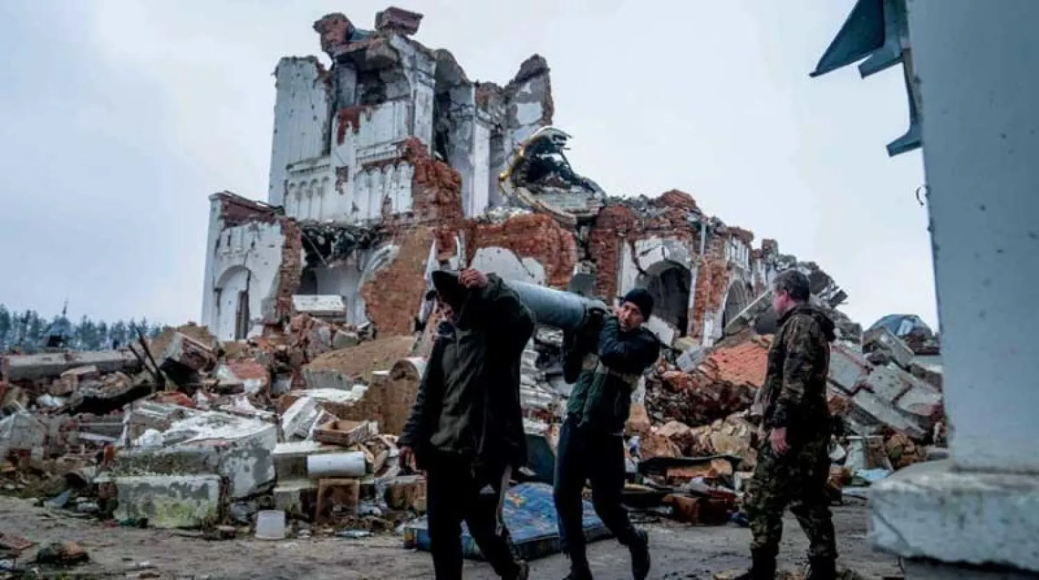 متطوعان يحملان بقايا صاروخ في أثناء تنظيف محيط كنيسة دمرت في قصف لقرية دوليما بمنطقة دونيتسك شرق أوكرانيا أمس (أ.ف.ب)