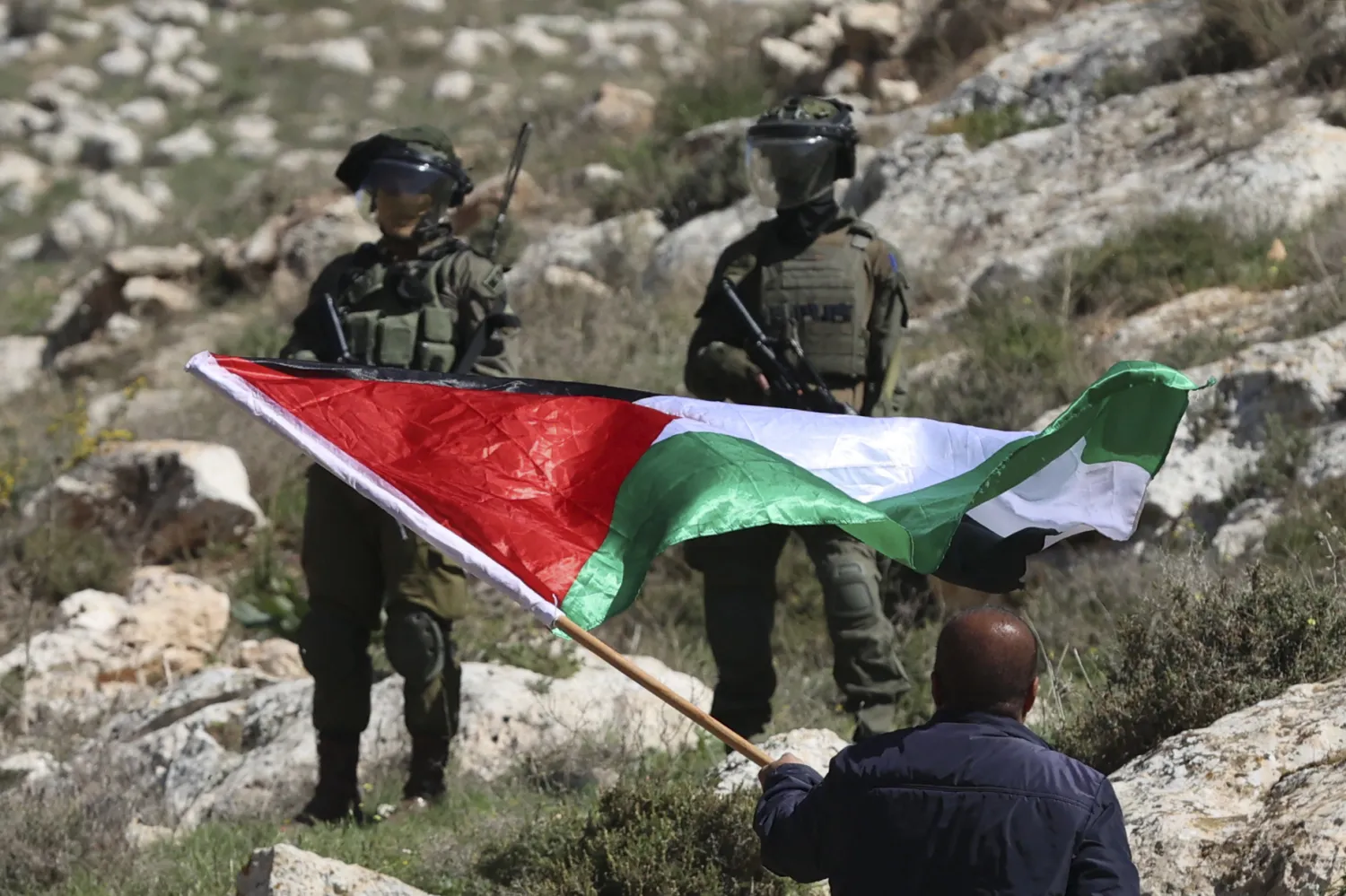 متظاهر فلسطيني يلوح بالعلم أمام القوات الإسرائيلية  بالقرب من مدينة نابلس في الضفة الغربية (أ.ف.ب)