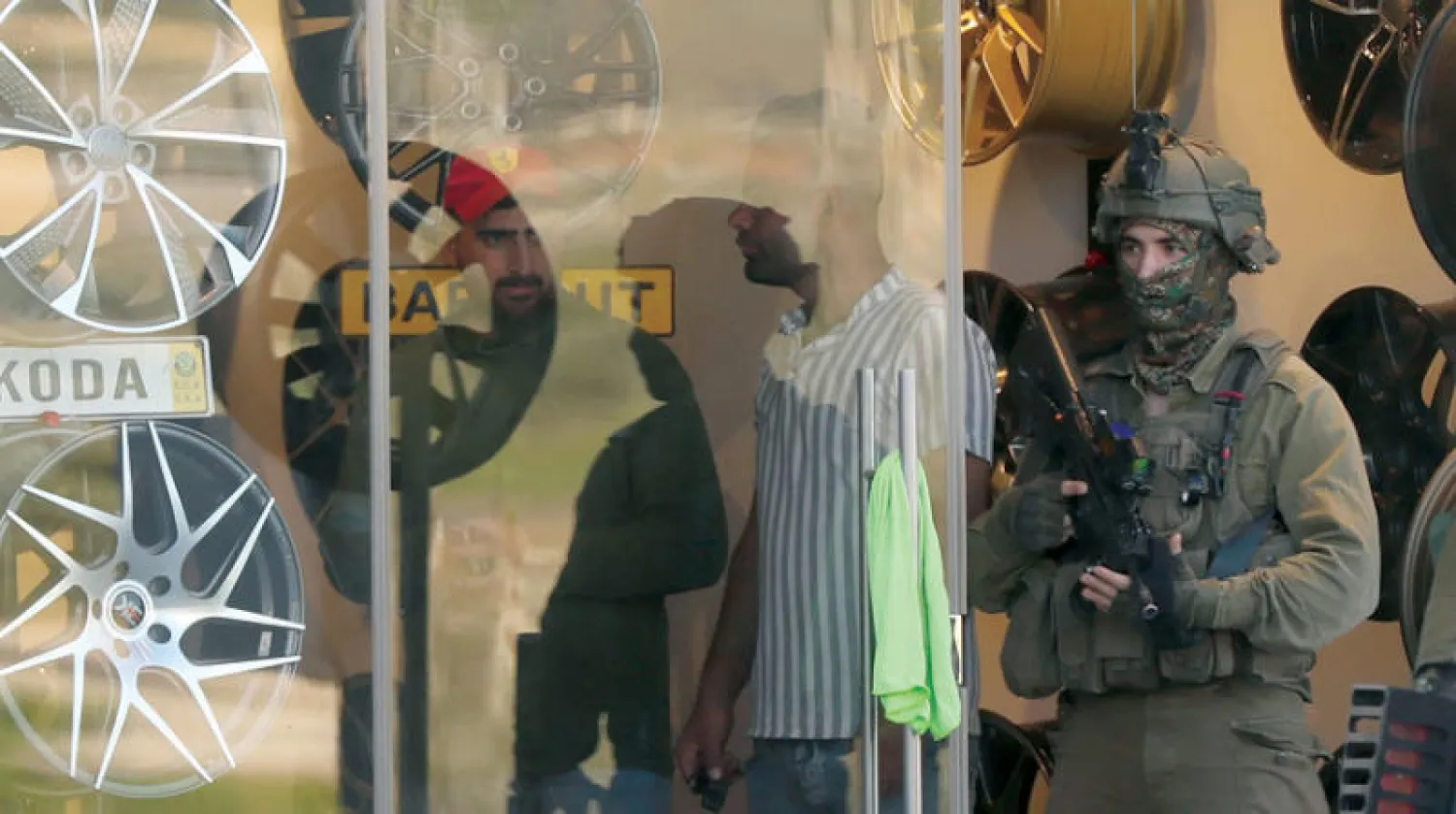 القوات الإسرائيلية تفتش متجراً في المنطقة التي قُتل فيها 3 فلسطينيين قرب حاجز صرة العسكري الأحد (إ.ب.أ)