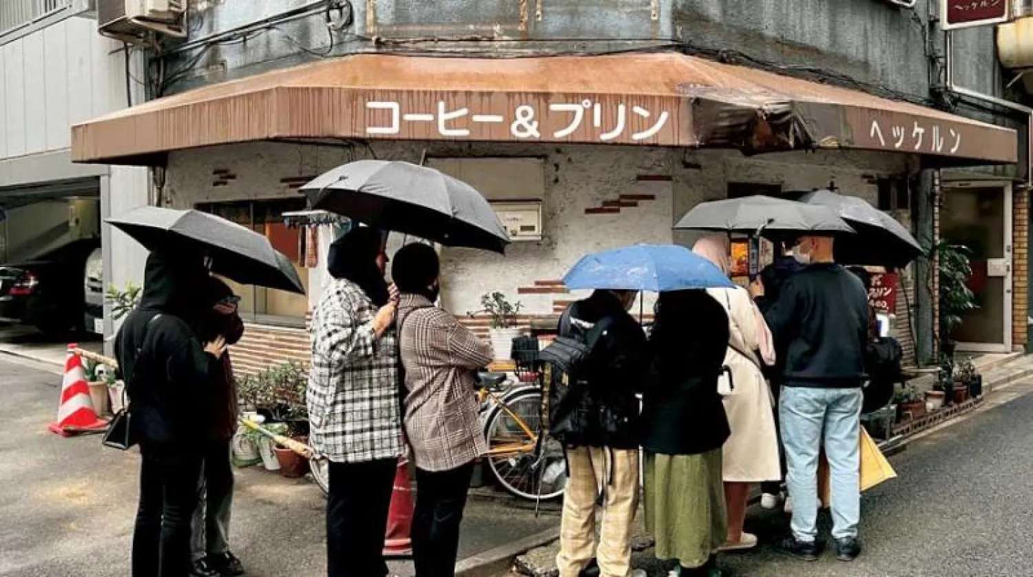 يابانيون يصطفون أمام محل لبيع القهوة في العاصمة طوكيو وسط أجواء ماطرة (رويترز)