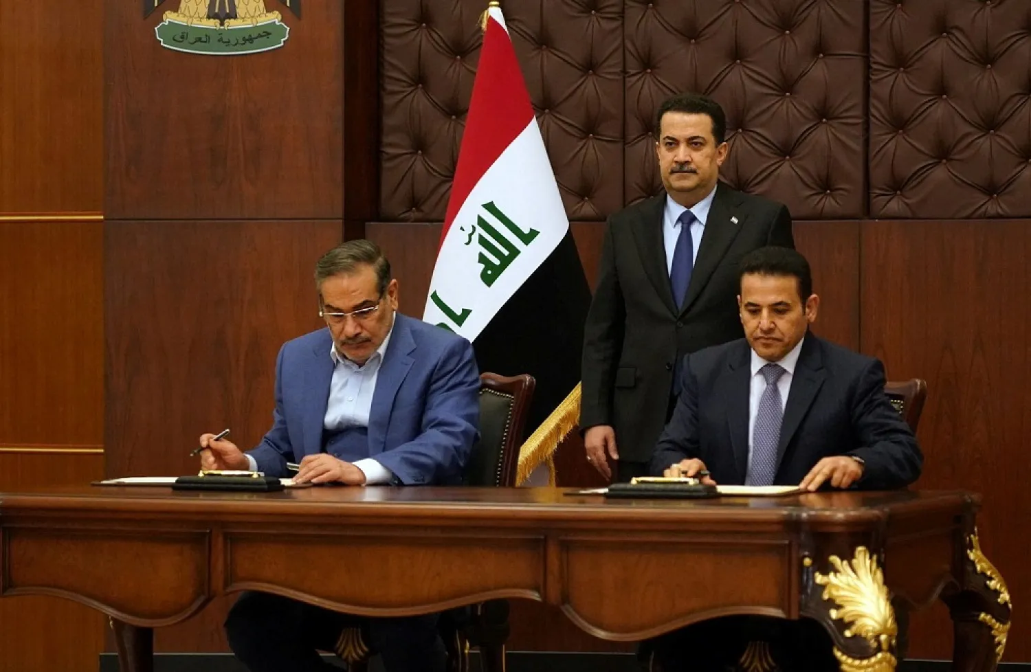 Iraqi Prime Minister Mohammed Shia al-Sudani looks on as Iraq's National Security Adviser Qasim al-Araji and Iran's Supreme National Security Council secretary Ali Shamkhani sign the security agreement that includes coordination in protecting the common borders between the two countries, in Baghdad, Iraq, March 19, 2023. (Iraqi Prime Minister Media Office/Handout via Reuters)
