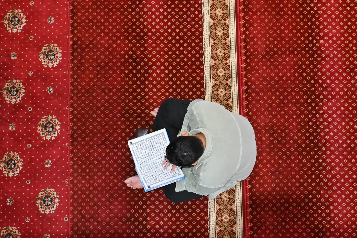 رجل يقرأ القرآن في مسجد المقمور في إندونيسيا (أ.ف.ب)