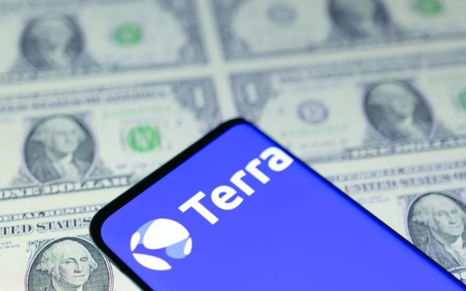 شعار منصة «تيرا» على أحد الهواتف الذكية وفي الخلفية عملات من فئات الدولار (رويترز)