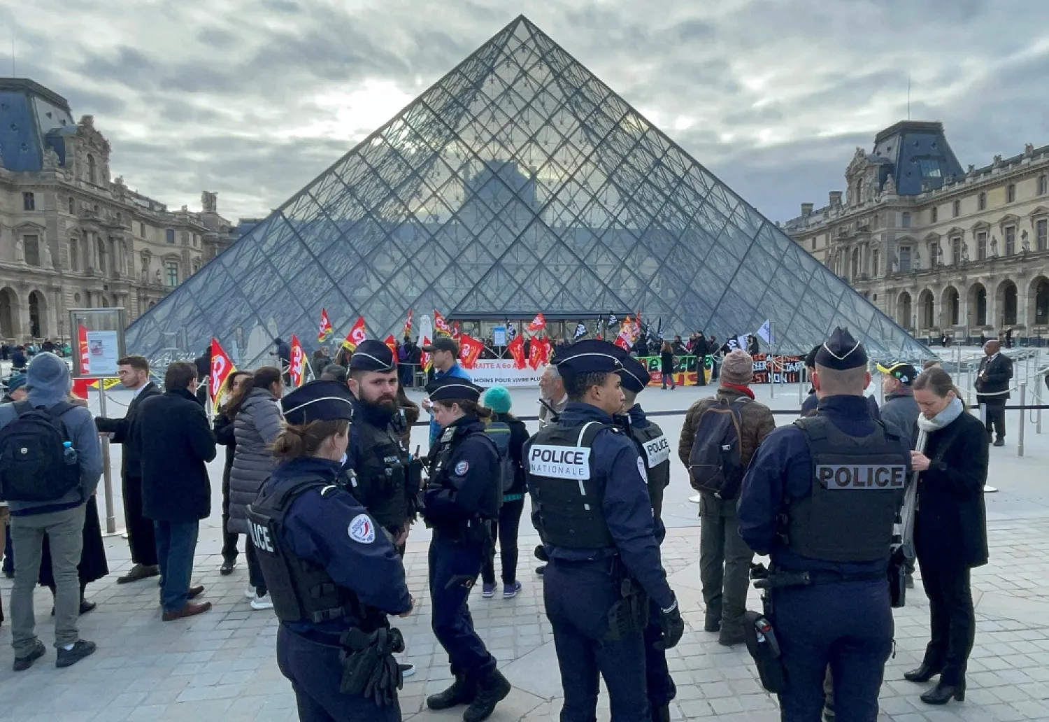 French police look on as protesters holding French CGT labor union flags in front of the glass Pyramid block the entrance of the Louvre museum to protest against the French government's pension reform, in Paris, France, March 27, 2023. (Reuters)