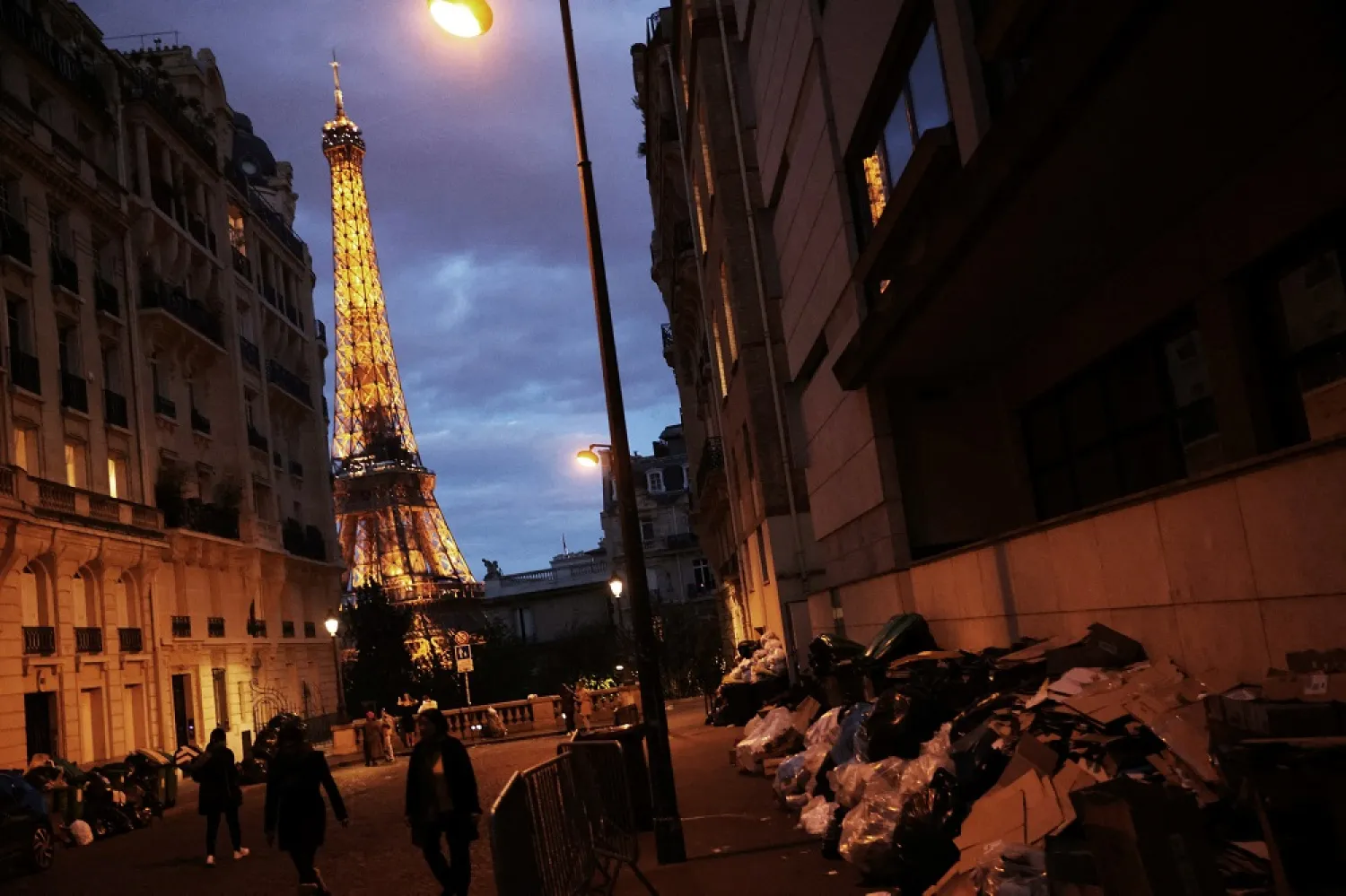 Tourists and locals walk past overflowing garbage bins in a street near the Eiffel Tower as garbage has not been collected due to a strike of garbage collectors against the French government pension reform, in Paris, France, March 27, 2023. (Reuters)