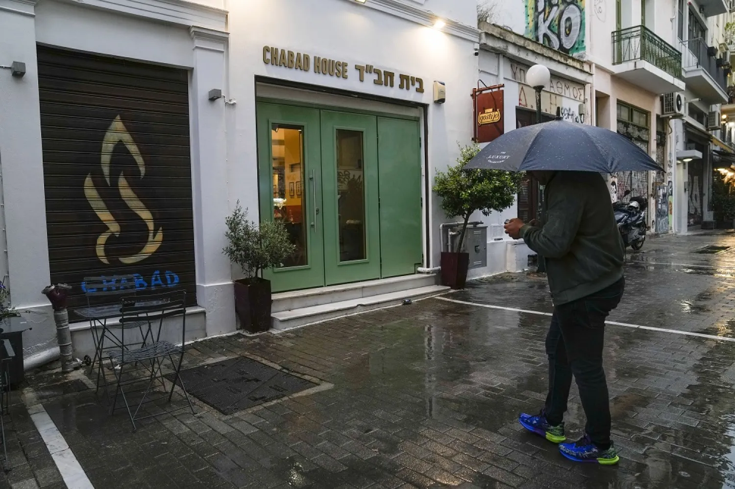 A man holding an umbrella stands in front of a Jewish restaurant that Greek officials believe was one of the targets of a planned terrorist attack, in central Athens, Tuesday, March 28, 2023. (AP)