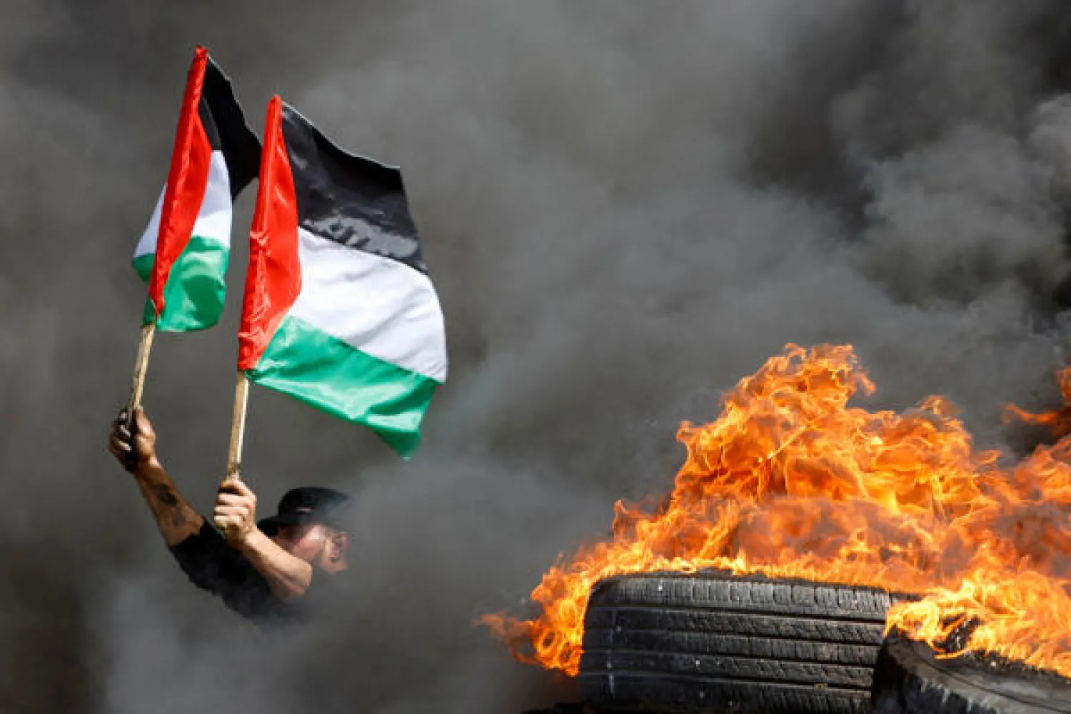 A demonstrator holds Palestinian flags next to burning tires during a protest over tension in Jerusalem, at the Israel-Gaza border fence, east of Gaza City April 5, 2023. REUTERS/Mohammed Salem TPX IMAGES OF THE DAY
