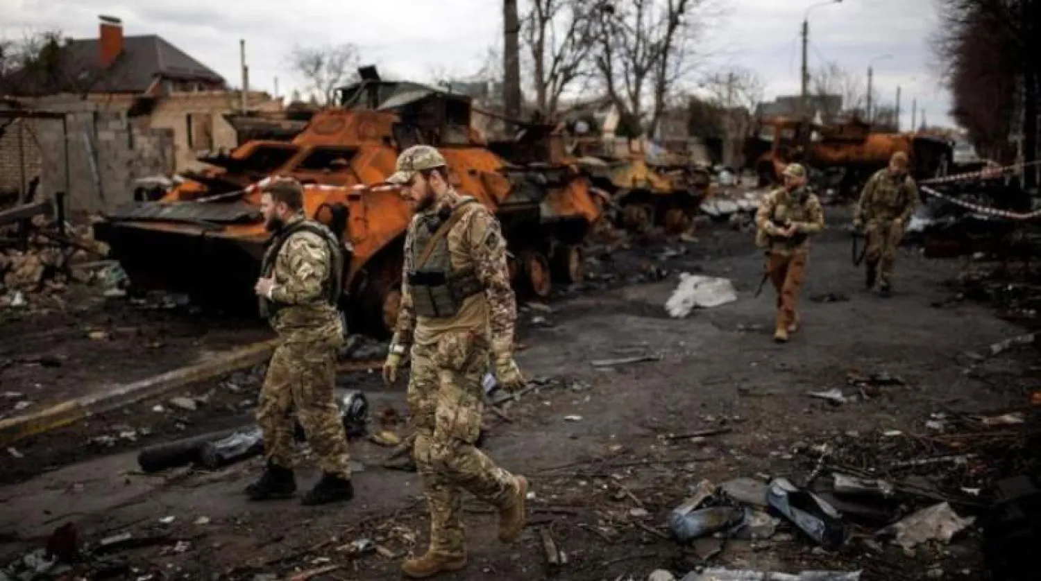 جنود أوكرانيون يسيرون جانب آليات روسية مدمرة في بوتشا بكييف  (رويترز)