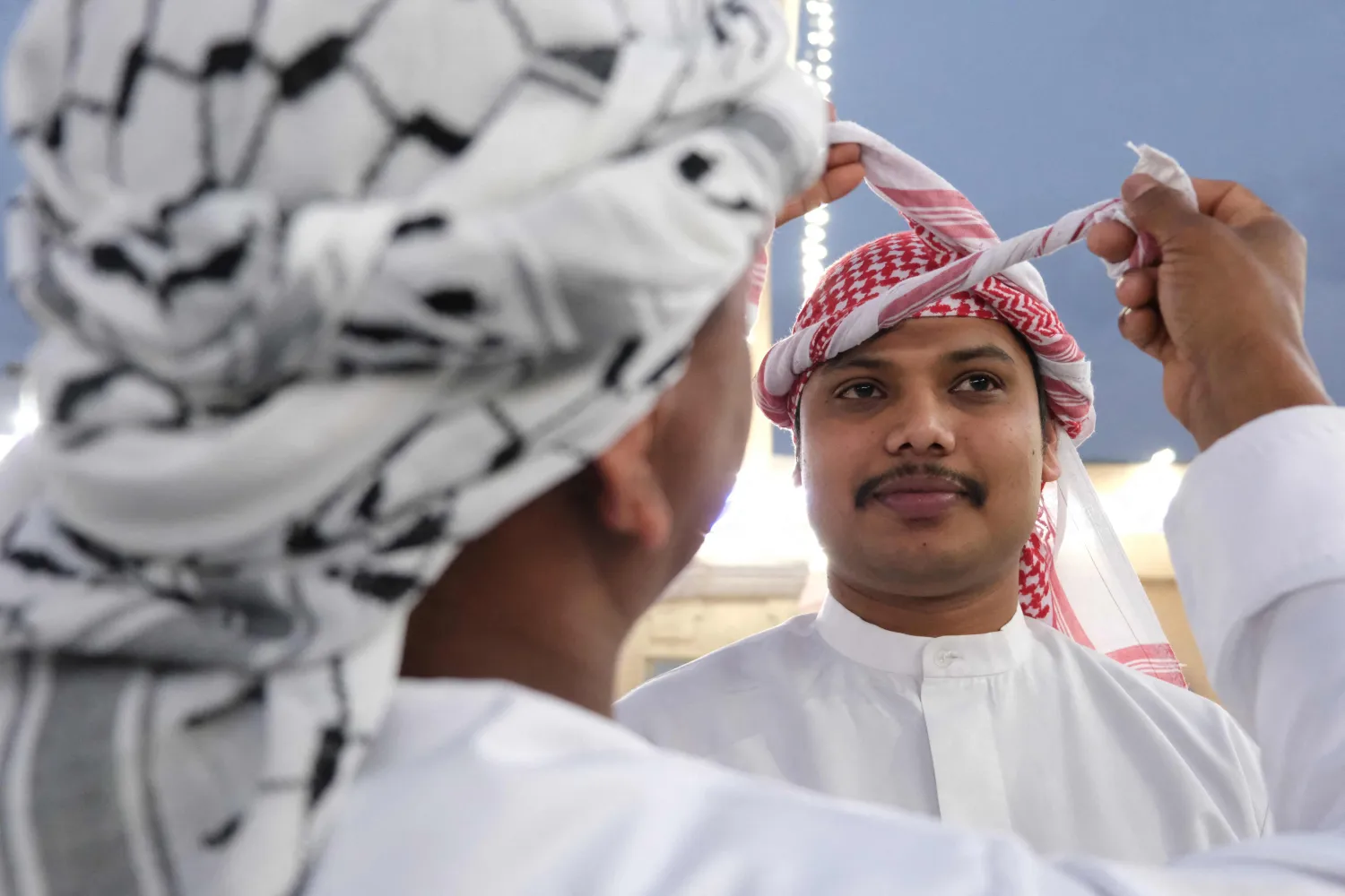 رجل يربط العقال لرجل آخر في أول أيام عيد الفطر في بغداد (أ.ف.ب)