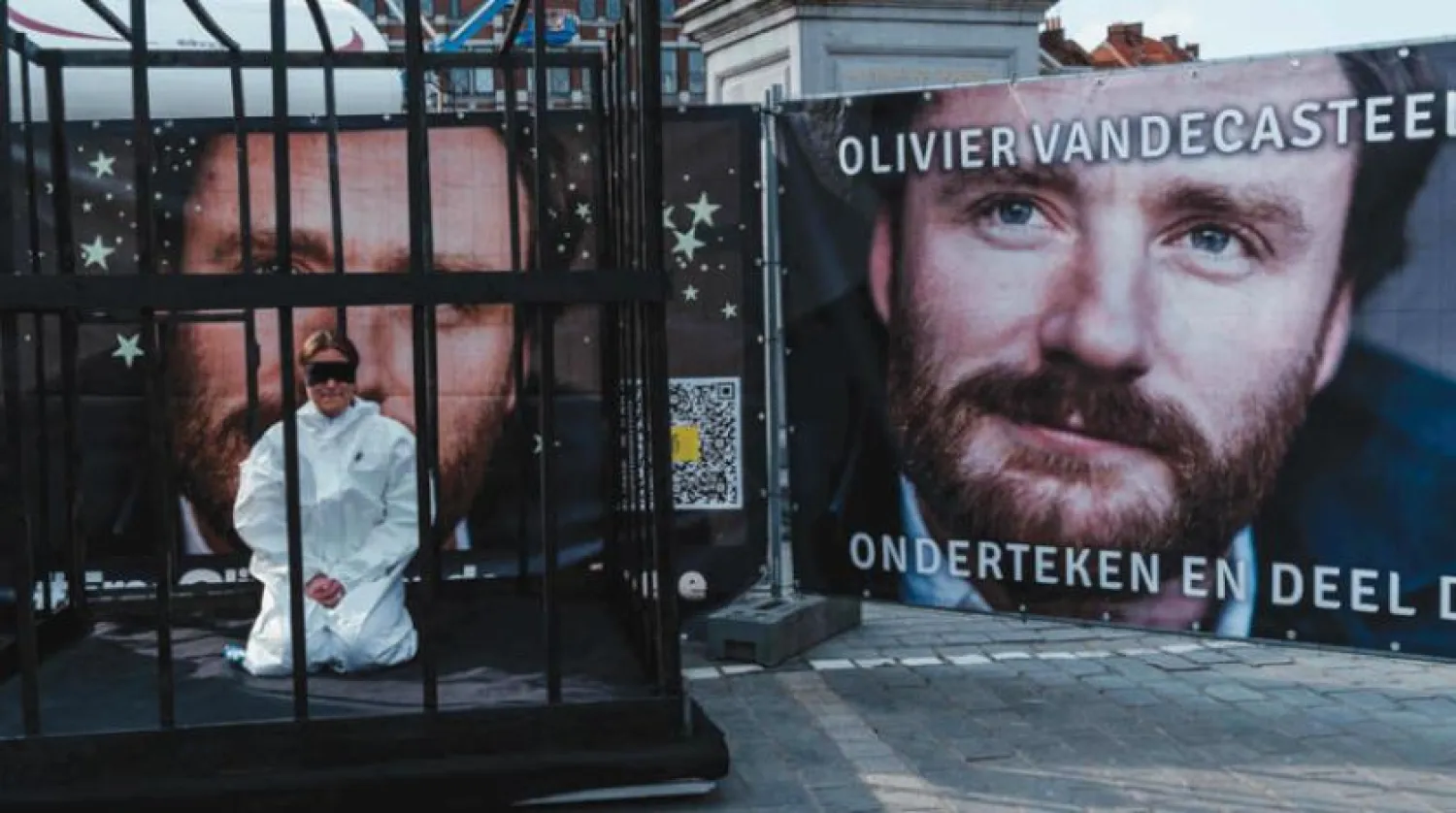 Brüksel’de İran tarafından tutuklanan Belçikalı insani yardım görevlisi Olivier Vandecasteele’nin posterinin yanındaki, demir parmaklıklar ardındaki bir protestocu. (AFP)