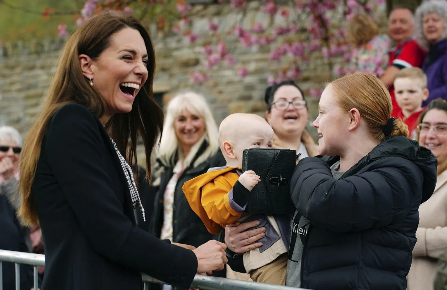 Lucy Williams, from Aberfan, holds her son Daniel as he takes the handbag from Britain's Kate, Princess of Wales during her visit with Prince William to the Aberfan memorial garden, Friday April 28, 2023. (AP)