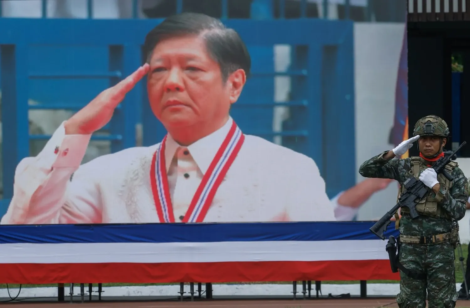 A police officer of the Special Action Force (R) salutes as Philippine President Ferdinand Marcos Jr. is projected on an electronic screen during Philippine National Police change of command ceremonies at Camp Crame police camp in Quezon City, Metro Manila, Philippines, 24 April 2023. (EPA)