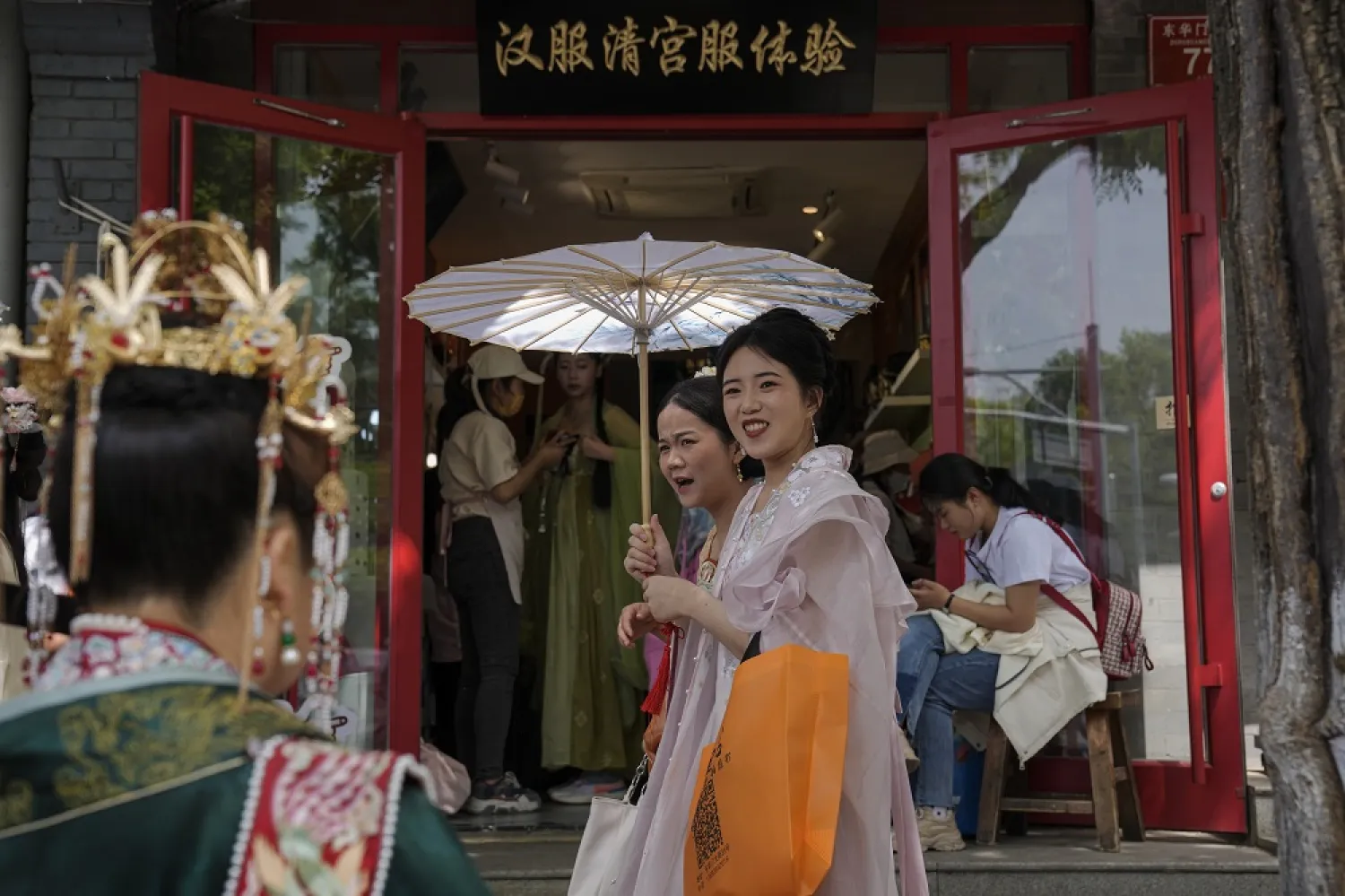 Women dressed in traditional costumes walk by vendors attend visitors at a shop renting traditional costumes near the Forbidden City during the May Day holiday period in Beijing, Tuesday, May 2, 2023. (AP)