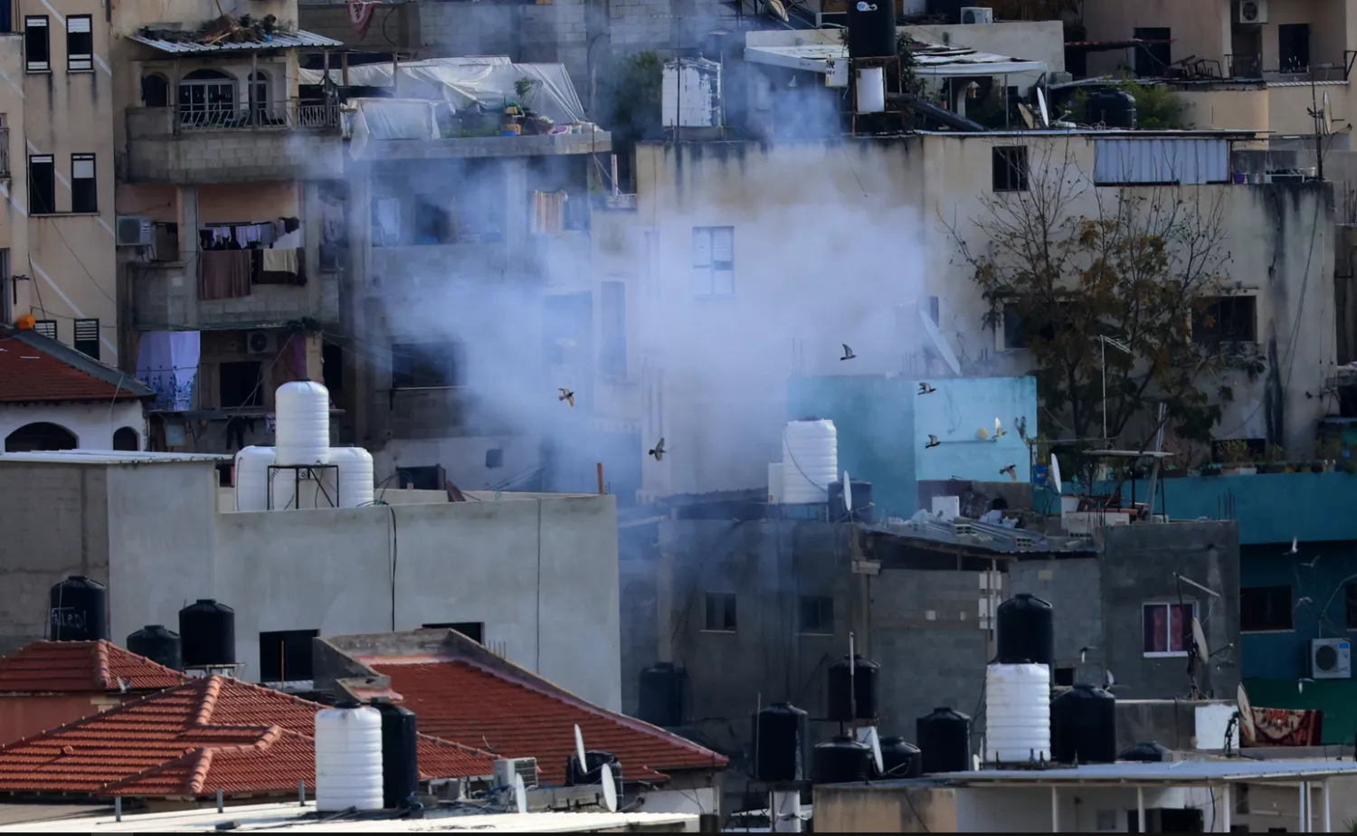 دخان يتصاعد خلال عملية عسكرية إسرائيلية على مخيم نور شمس للاجئين بالقرب من مدينة طولكرم بالضفة الغربية (إ.ب.أ)