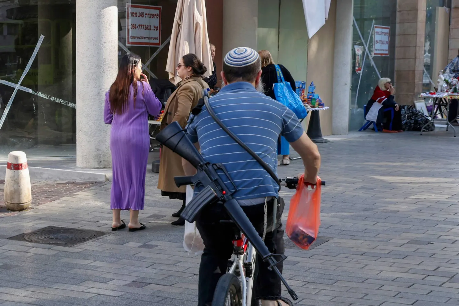 مواطن إسرائيلي على متن دراجة هوائية وهو يحمل السلاح في مدينة نهاريا الإسرائيلية (أ.ف.ب)