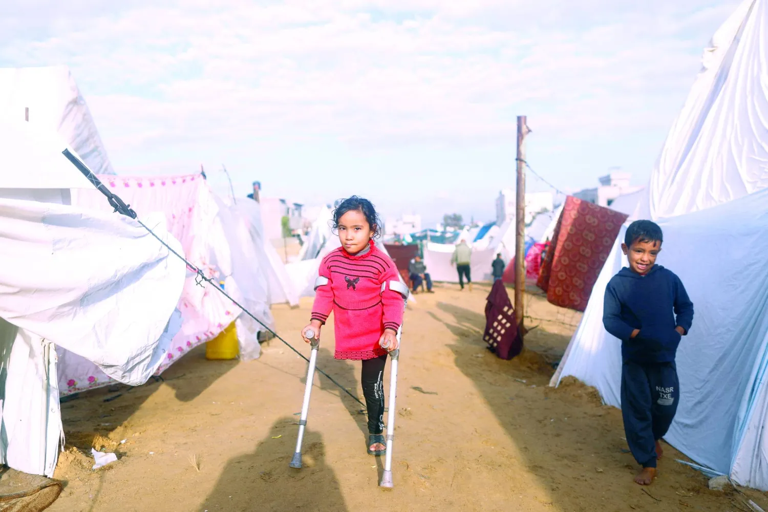 
طفلة فلسطينية تمشي متكئة على عكاز وسط مخيم للنازحين في رفح جنوب قطاع غزة أمس (رويترز)