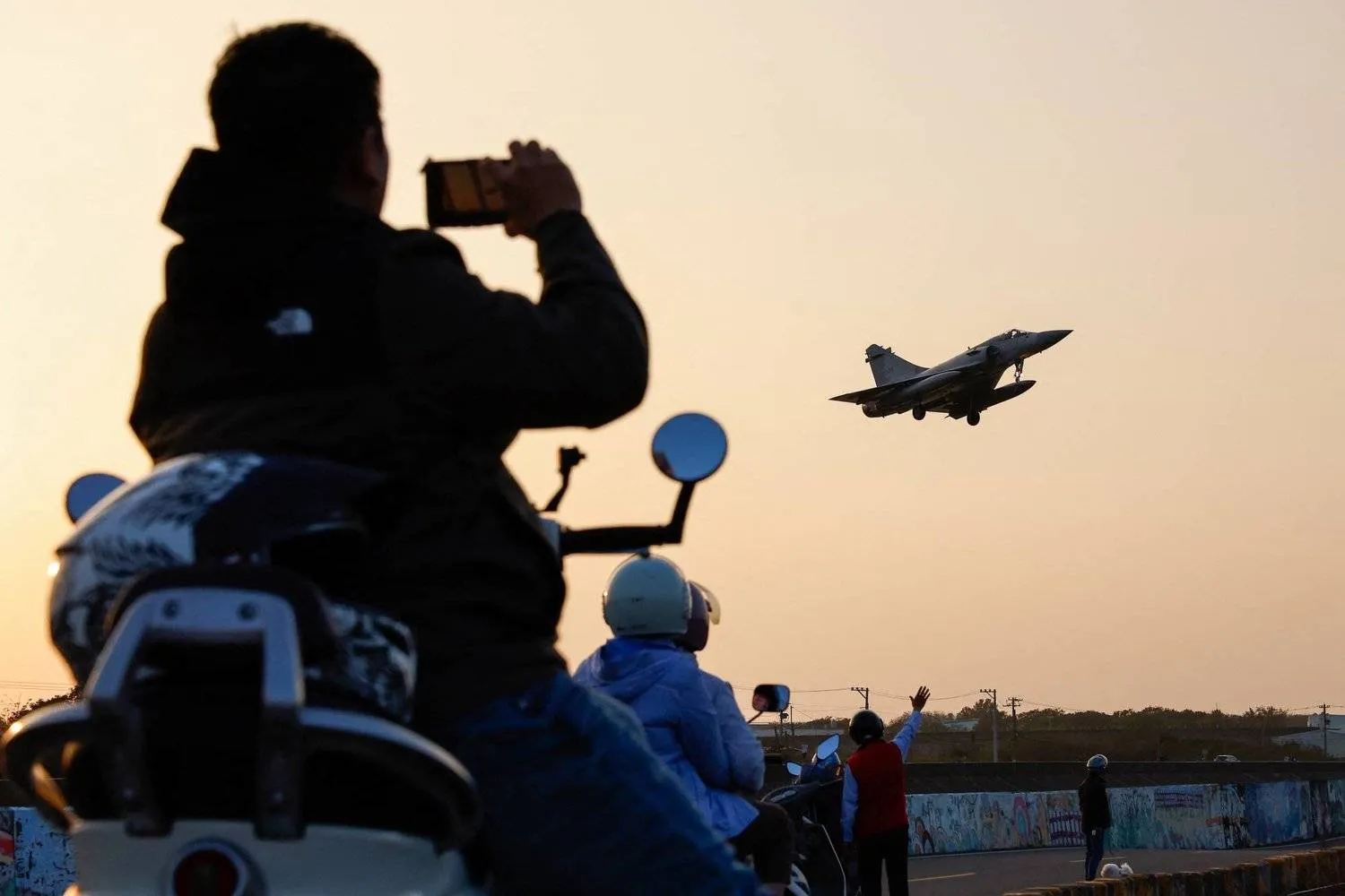 A person uses a phone while people look at a Taiwan Air Force plane preparing to land at Hsinchu Base (Reuters)