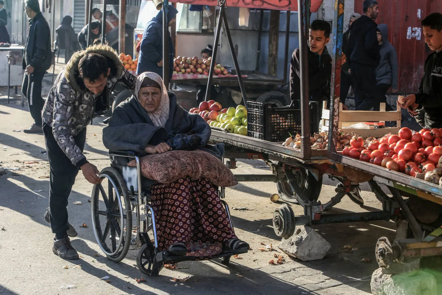 يساعد فلسطينية على كرسي متحرك في مدينة رفح اليوم (د.ب.أ)