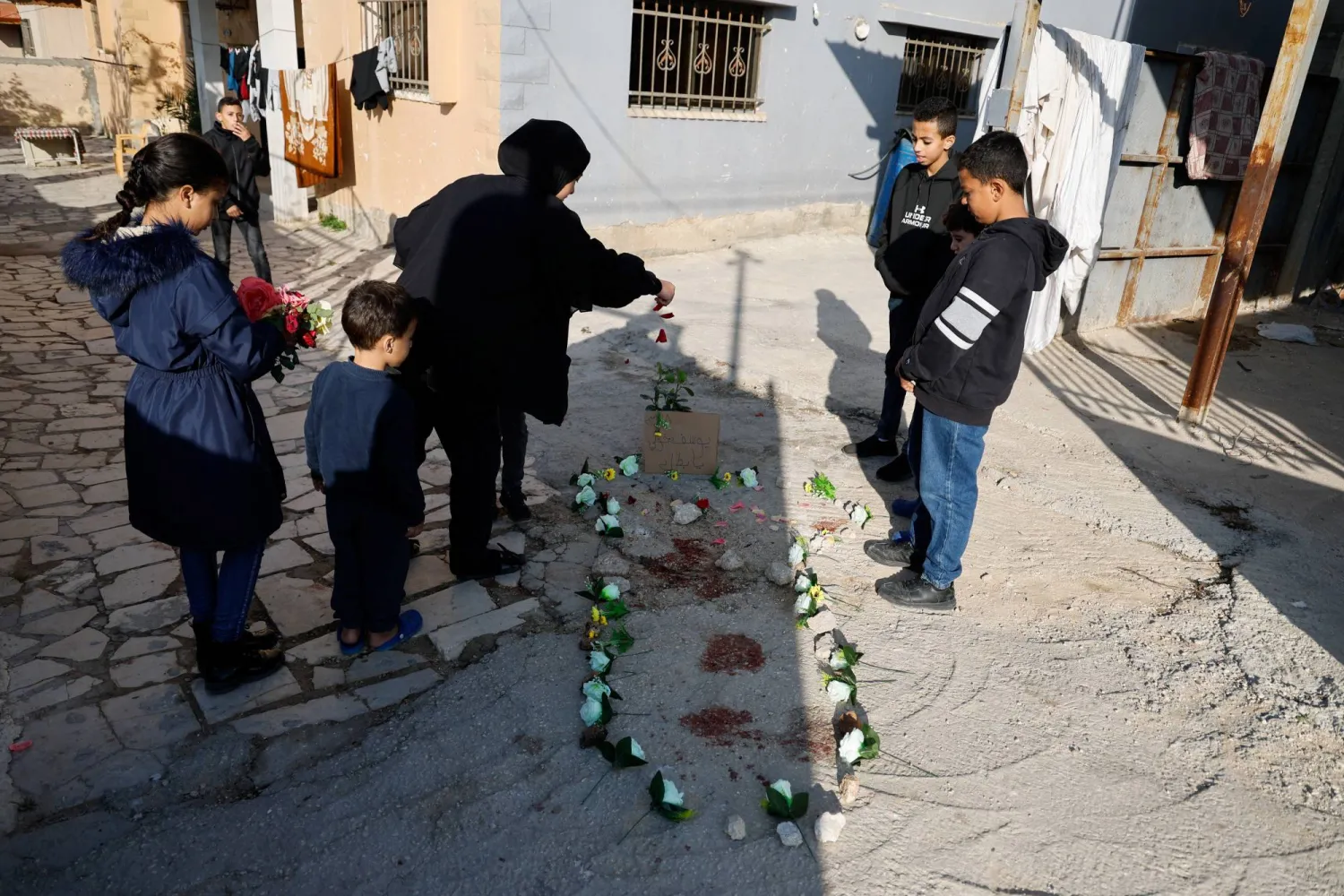 أهالي فلسطينيون يضعون الزهور حول بقع الدم في موقع الدهس في طولكرم (رويترز)