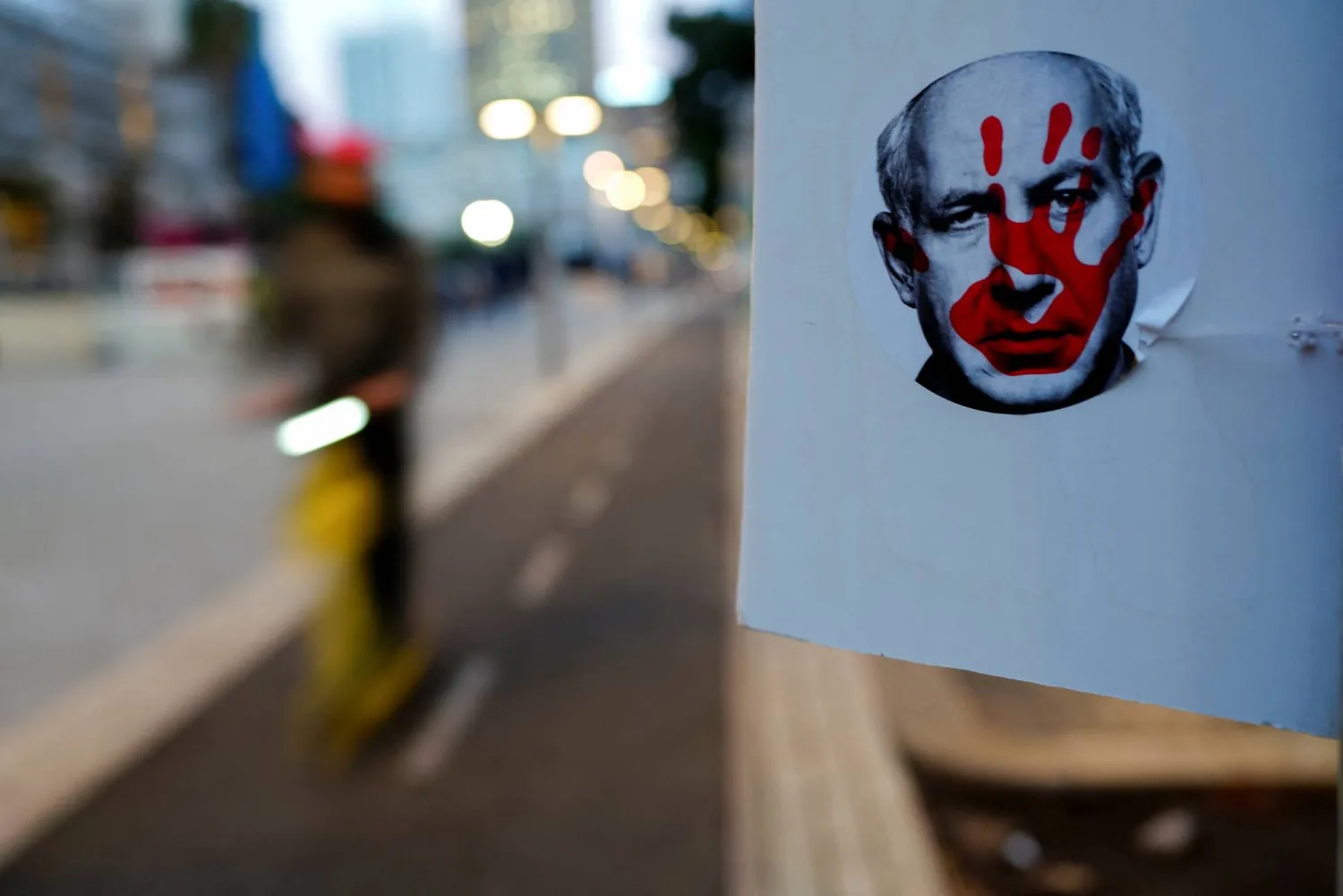 A man rides a scooter past a sticker depicting Israeli Prime Minister Benjamin Netanyahu, in a street in Tel Aviv, Israel January 2, 2024. REUTERS/Alexandre Meneghini