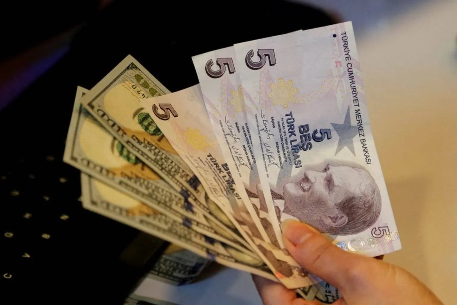 A money changer holds Turkish lira and US dollar banknotes at a currency exchange office in Ankara, Türkiye December 16, 2021. (Reuters)
