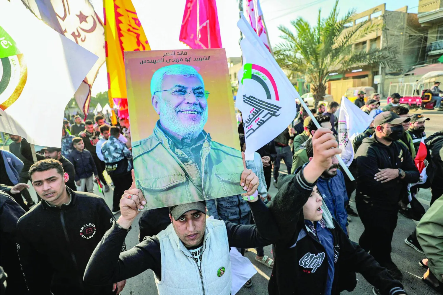 مجموعة من أنصار الفصائل العراقية يحملون صورة المهندس وشعار «الحشد الشعبي» في بغداد (أ.ف.ب)