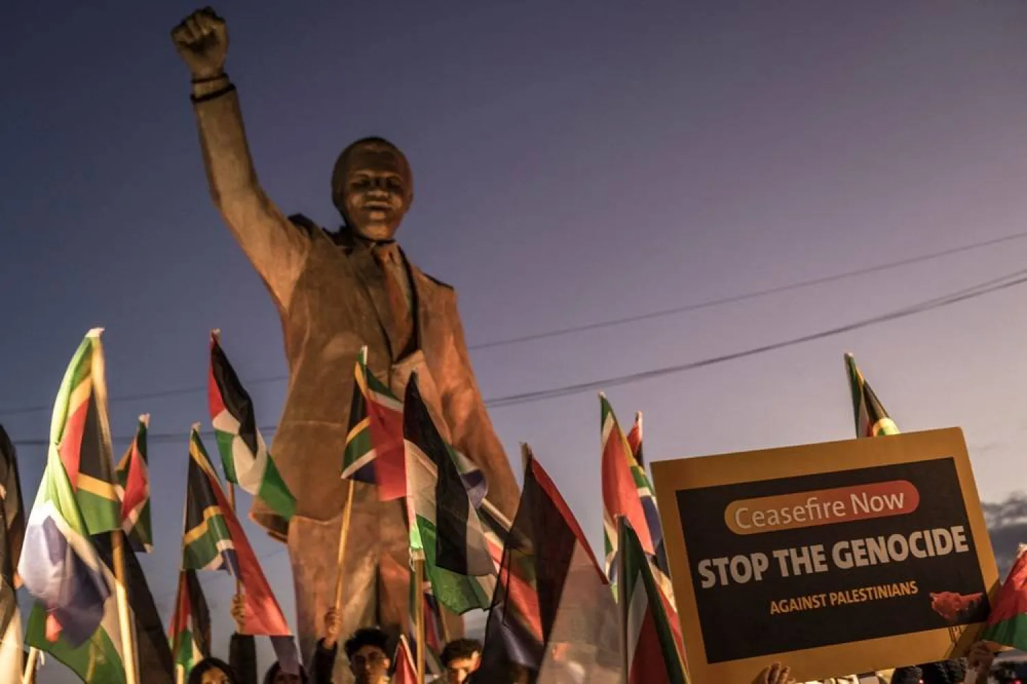 People raise flags and placards as they gather around a statue of late South African president Nelson Mandela to celebrate a landmark "genocide" case filed by South Africa against Israel at the International Court of Justice, in the occupied West Bank city of Ramallah on January 10, 2024. (AFP)