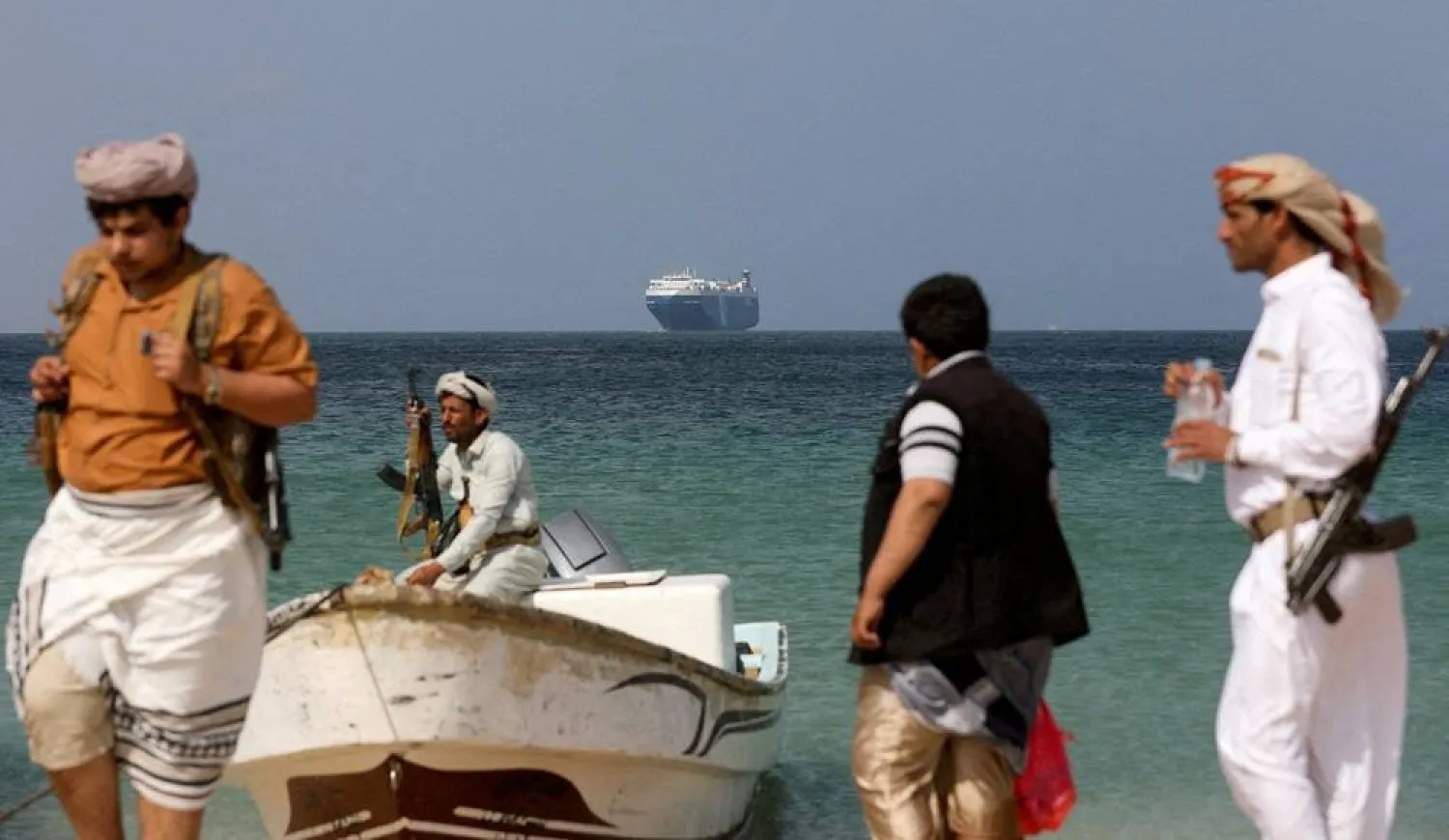 Armed men stand on the beach as the Galaxy Leader commercial ship, seized by Yemen's Houthis last month, is anchored off the coast of al-Salif, Yemen, December 5, 2023. (Reuters)