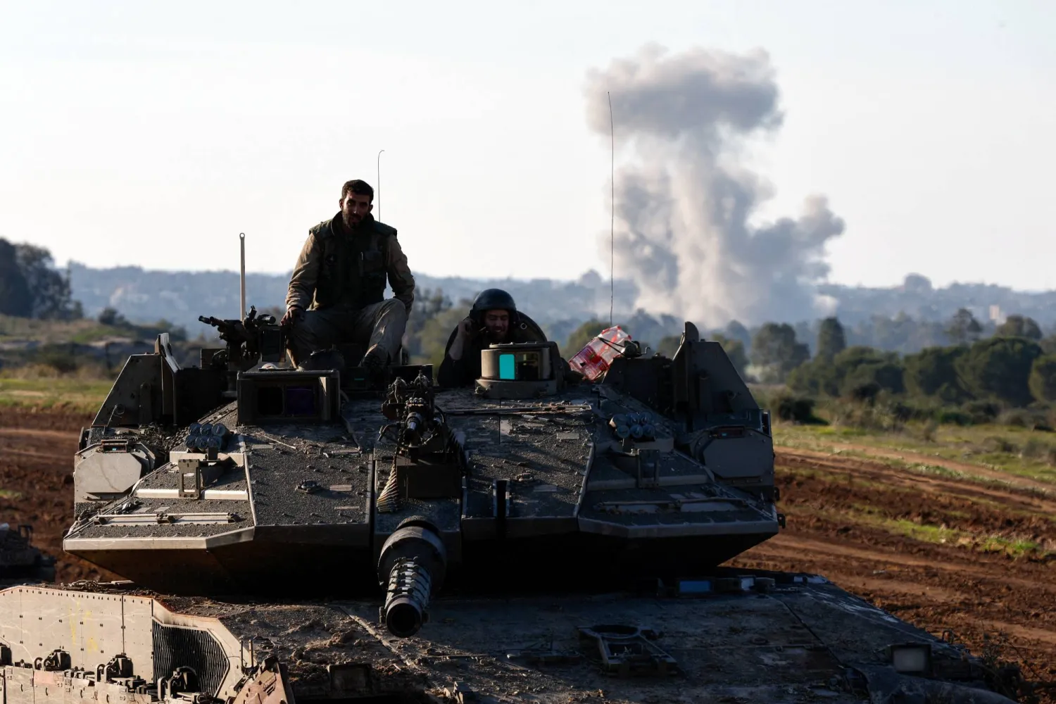 الدخان يتصاعد على مسافة بينما يقود جنود إسرائيليون دبابة أثناء خروجهم من قطاع غزة (رويترز)