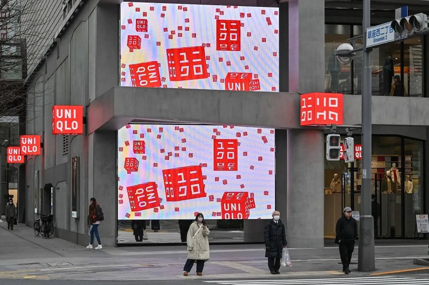 Pedestrians wait to cross the street outside a branch of the Fast Retailing clothing brand Uniqlo along a street in Tokyo on January 11, 2024. (AFP)