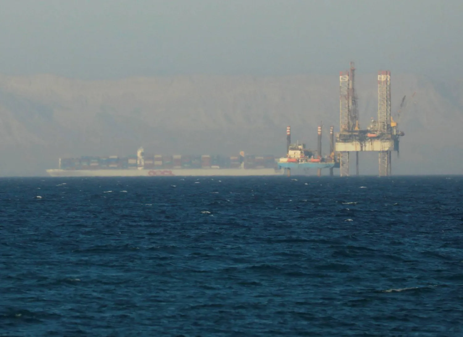 سفينة حاويات تعبر منصة نفطية في خليج السويس باتجاه البحر الأحمر (رويترز)