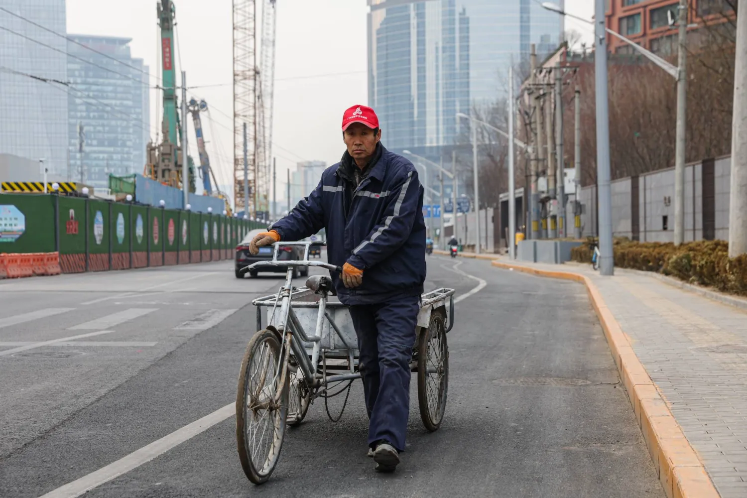 A man pushes a tricycle beside a construction site in Beijing, China, 17 January 2024. EPA/WU HAO