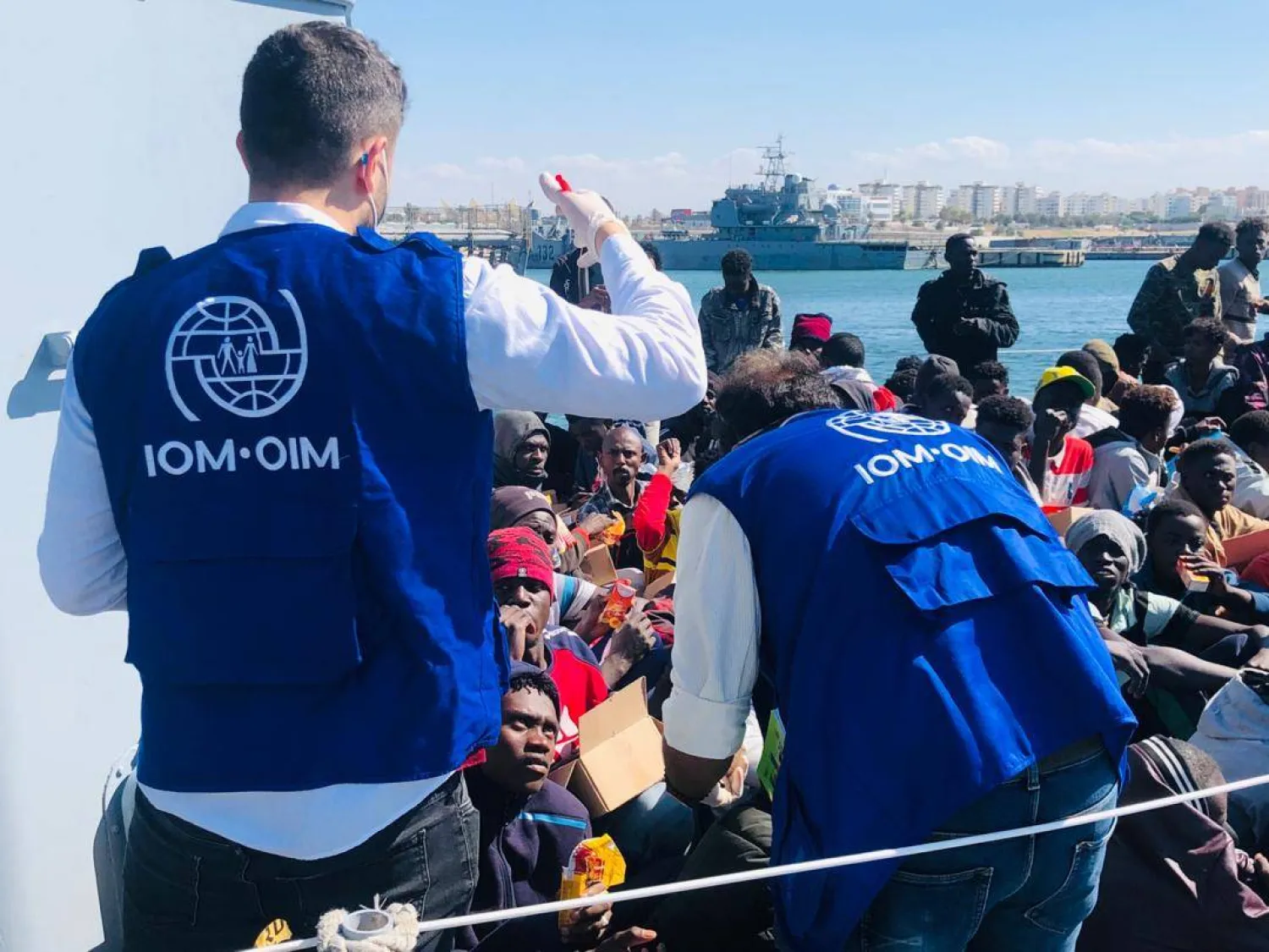 موظفان من المنظمة الدولية للهجرة يساعدان مهاجرين أعادهم خفر السواحل الليبي إلى طرابلس (أرشيفية - منصة «إكس»)