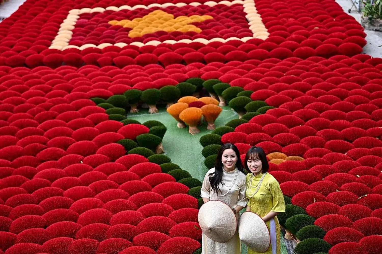 In this photo taken on January 20, 2024 tourists pose in front of incense sticks arranged in the form of a Vietnamese map and flag in a courtyard in the village of Quang Phu Cau on the outskirts of Hanoi. (AFP)